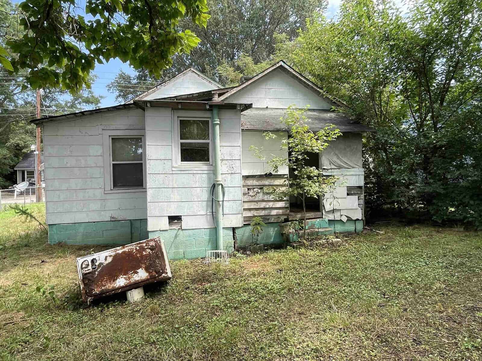 An old, neglected house with peeling paint and overgrown vegetation.