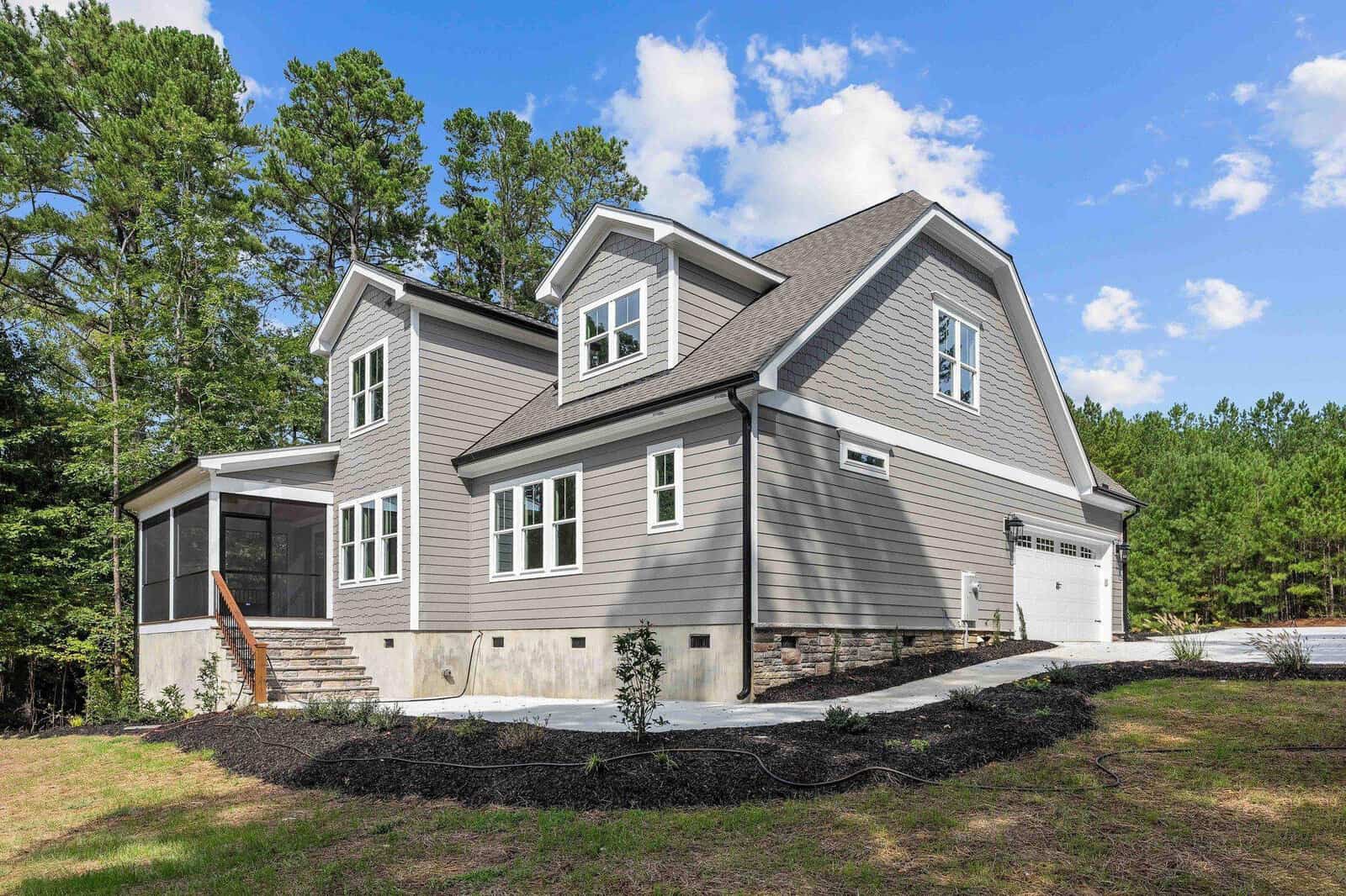 Two-story suburban home with grey siding and a garage under a clear sky.