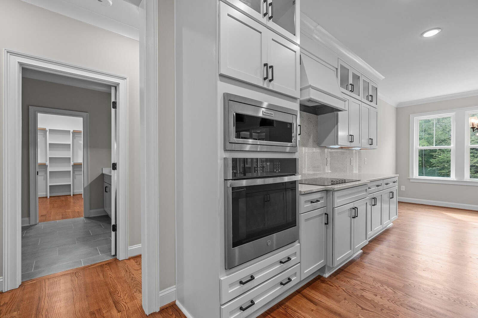 A modern kitchen with stainless steel appliances, white cabinetry, and hardwood floors, featuring a view of adjacent rooms.