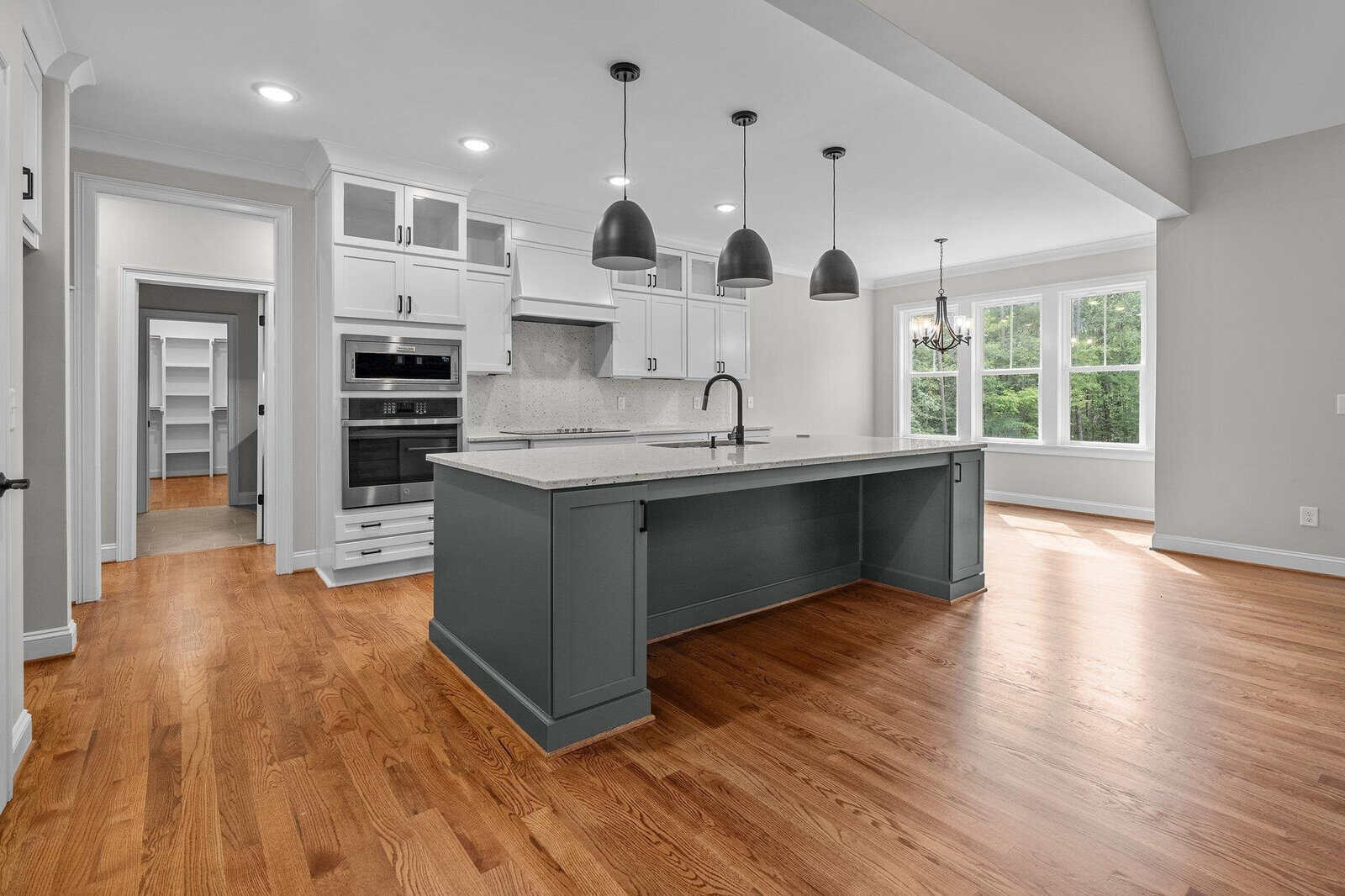 Modern kitchen with white cabinetry, stainless steel appliances, hardwood floors, and a gray island under pendant lights.