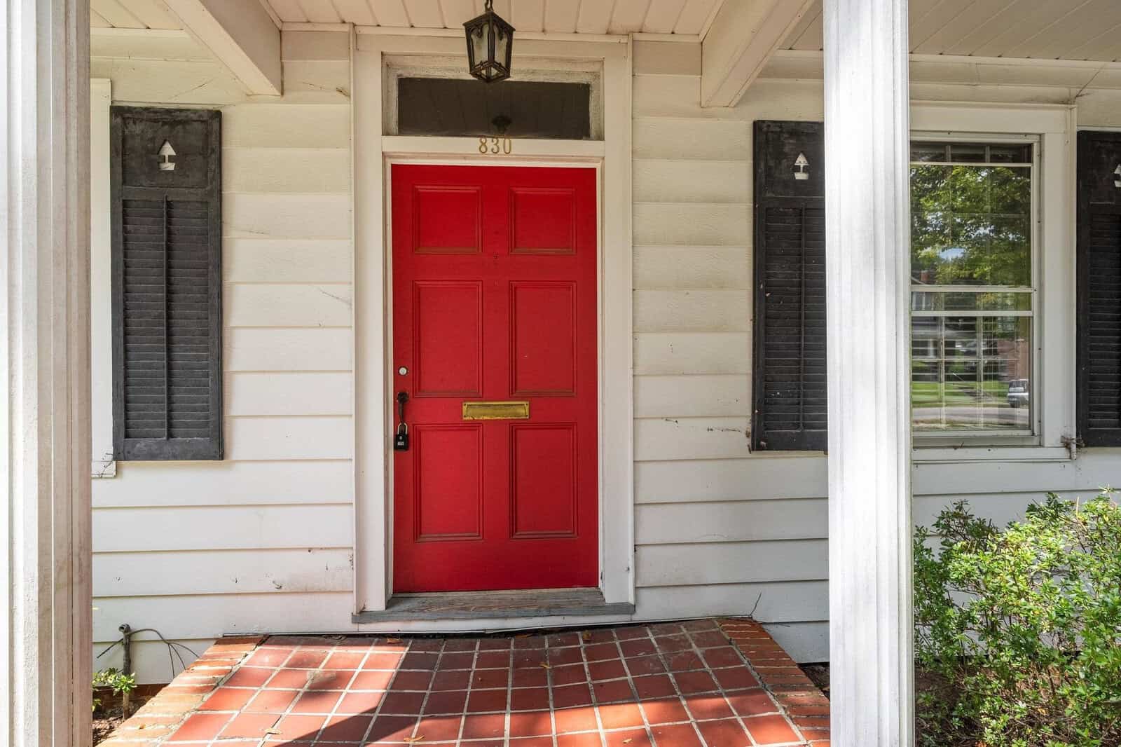 A red front door on a white house, flanked by black shutters, with a brick entryway.