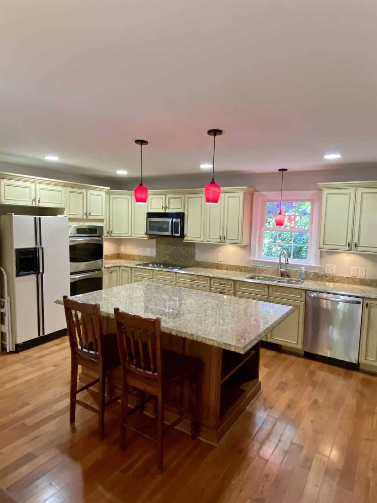 A modern kitchen with stainless steel appliances, granite countertops, and a central island under pendant lights.