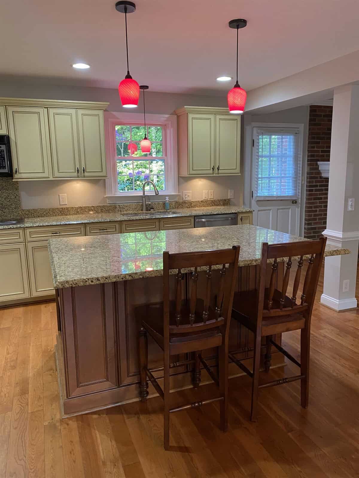 A modern kitchen featuring an island with a granite countertop and bar stools, complemented by red pendant lights and traditional cabinetry.