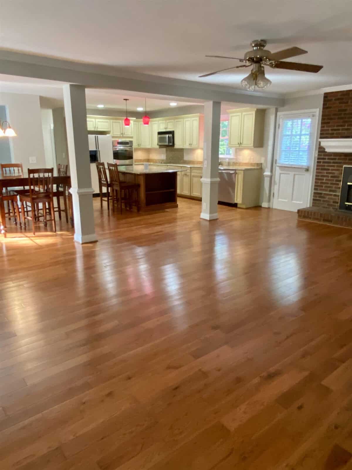 An open-concept living space with hardwood floors, featuring a kitchen with white cabinetry and a dining area in the background.