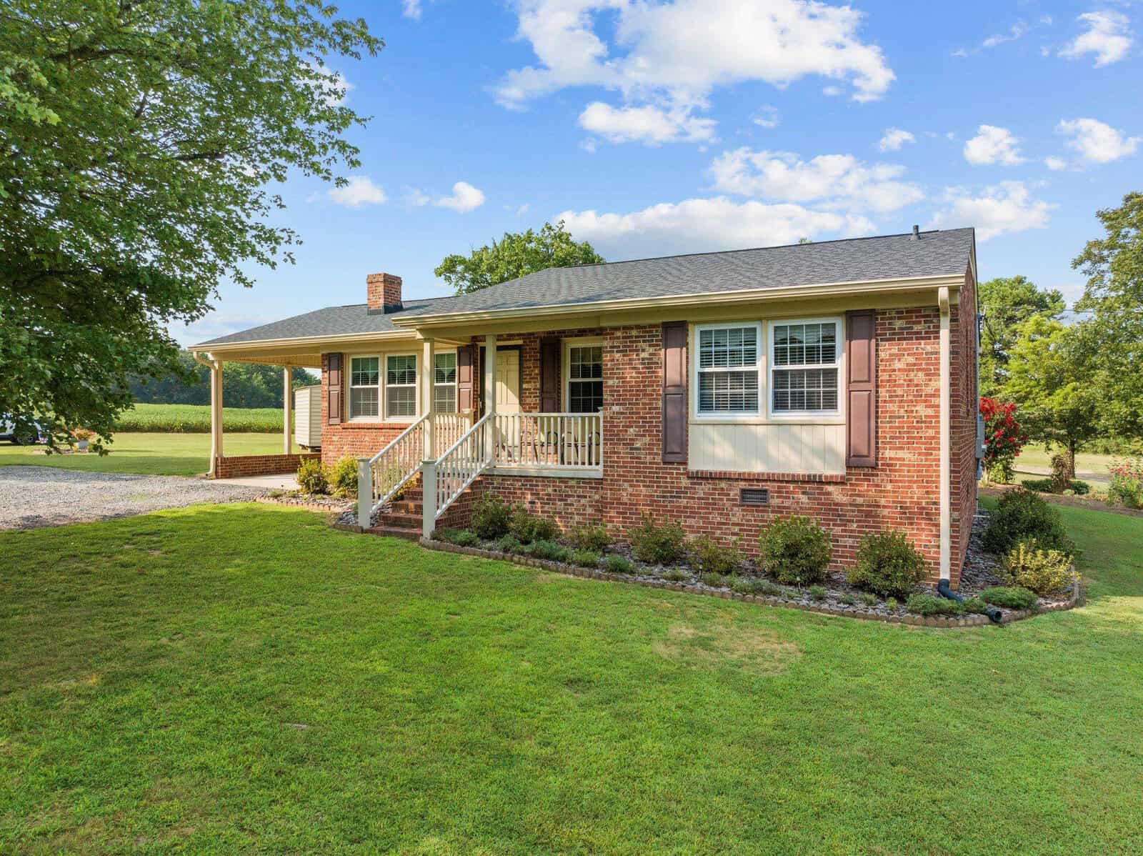 A charming brick house on 5953 Hicksboro Road features a covered front porch, surrounded by a well-maintained lawn and shrubs. The clear, sunny sky over Oxford adds to its inviting atmosphere.