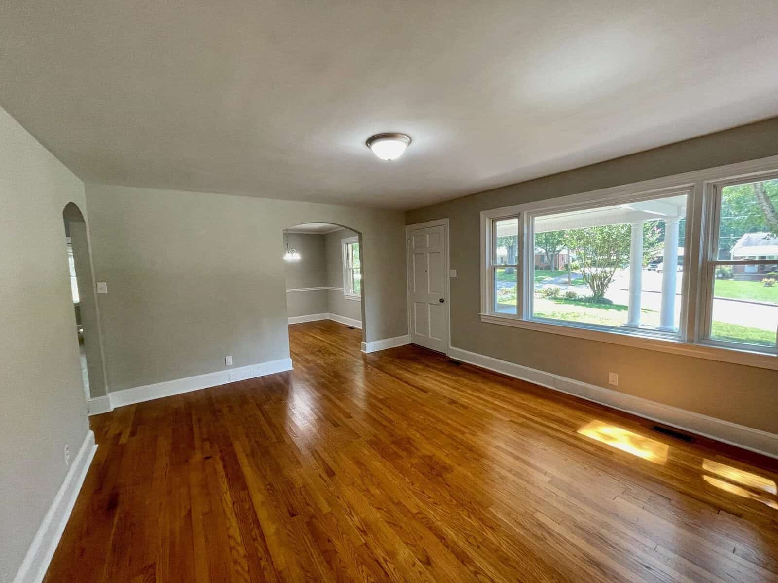 A well-lit, empty room with glossy hardwood floors, white walls, and multiple windows allowing natural light in.