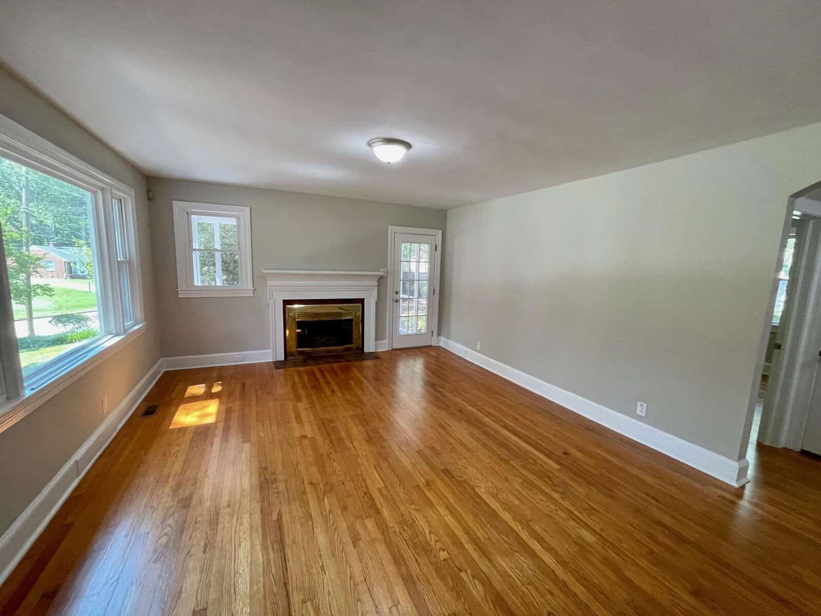An empty living room with polished wooden floors, white walls, a fireplace, and a set of french doors on the right.