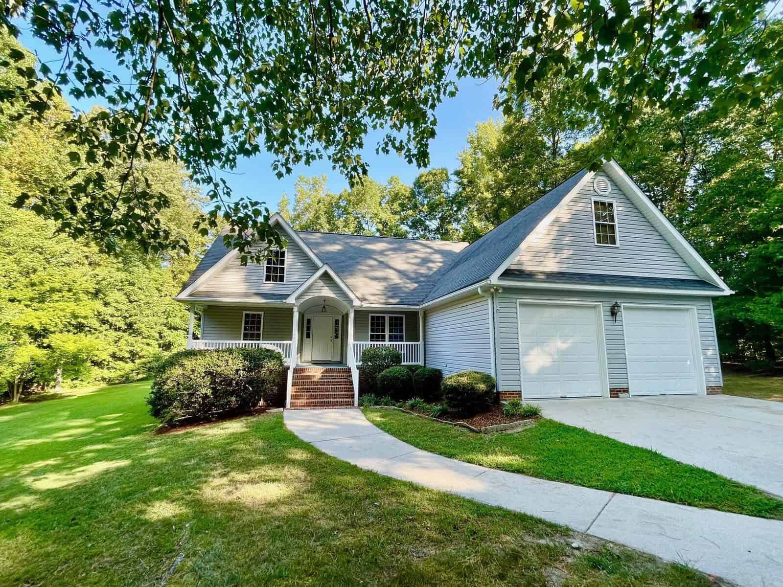 A single-family house at 119 Canterbury Court, Henderson NC, with a gabled roof, white siding, and an attached garage, nestled among greenery on a sunny day.
