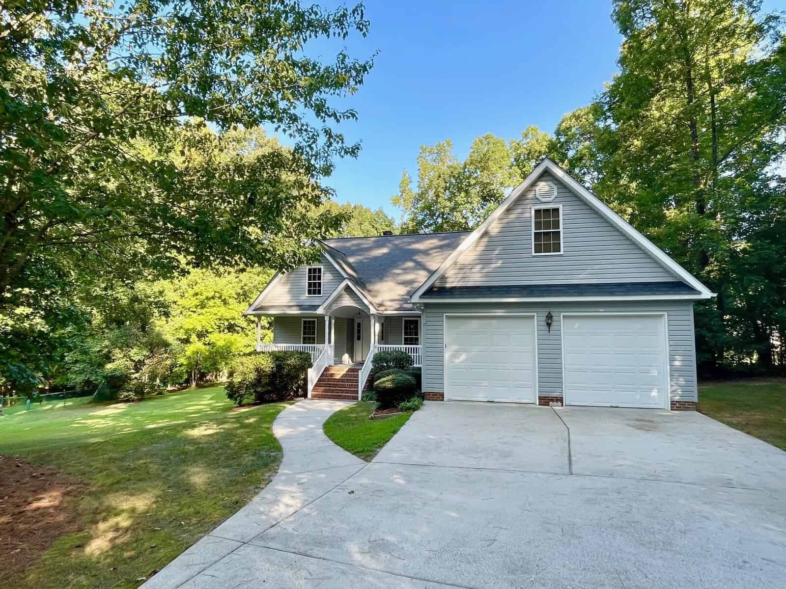 A two-story house with a white exterior, gable roof, and a two-car garage, surrounded by trees and a manicured lawn.