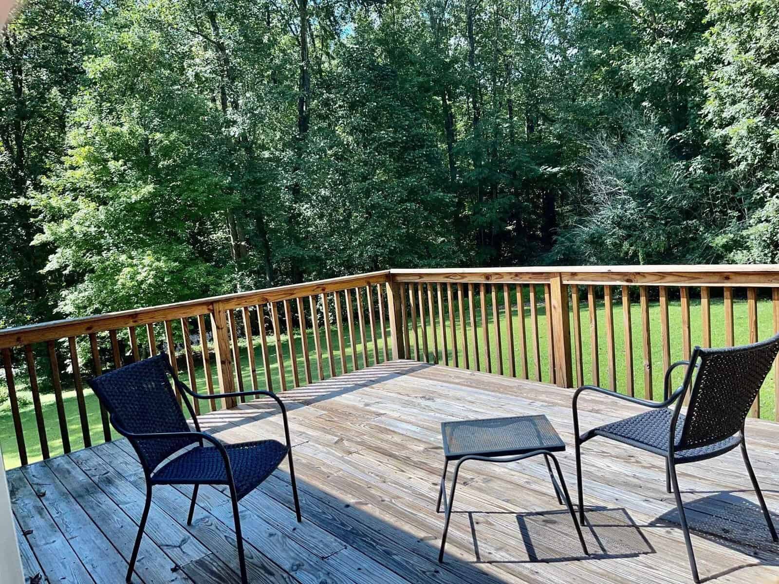 A wooden deck with two black chairs overlooking a lush green backyard bordered by a wooden railing.