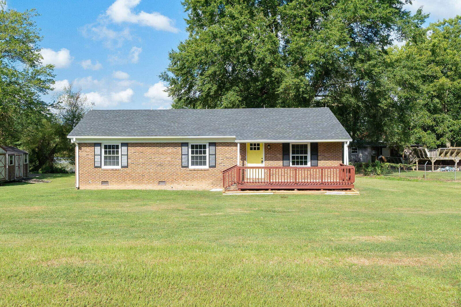 A single-story brick house with a red wooden front deck and a large green lawn under a clear sky, located at 88 Franklin Road, Henderson NC.