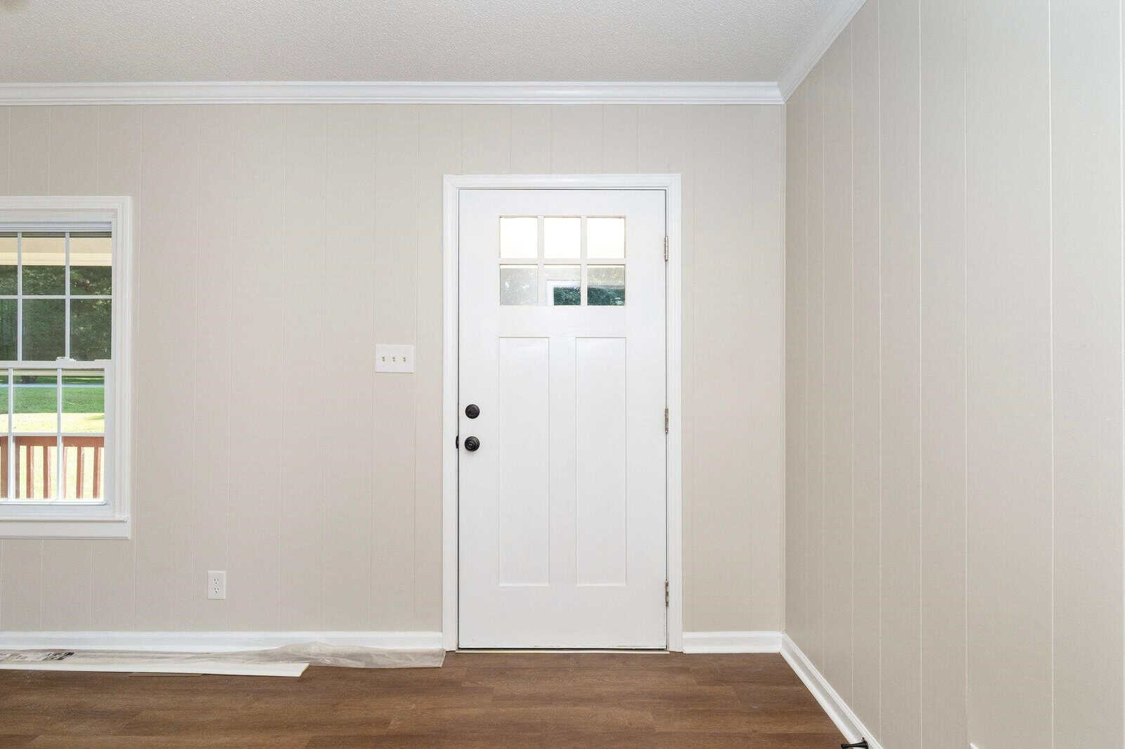 An empty room with beige walls, dark brown flooring, and a white door with a window.
