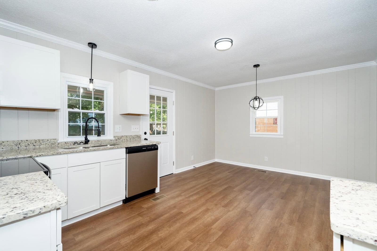 A spacious, modern kitchen with white cabinetry, granite countertops, stainless steel appliances, and hardwood flooring.