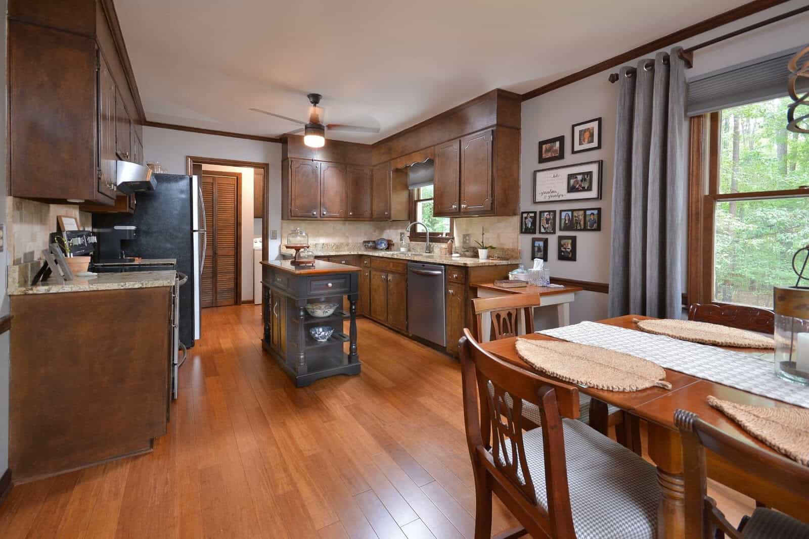A spacious kitchen with wooden cabinets, stainless steel appliances, and hardwood flooring, extending into a dining area with a set table.