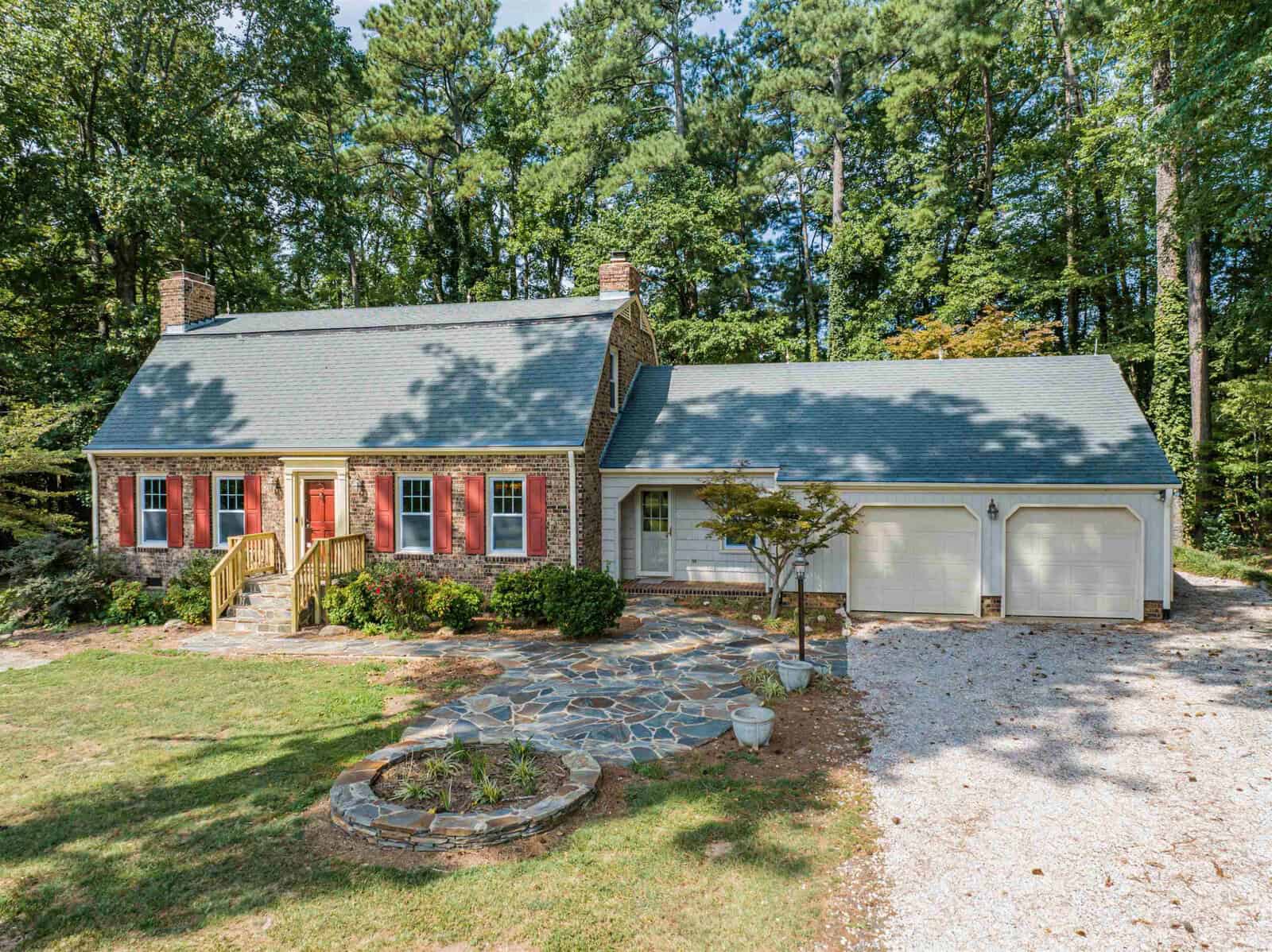 A single-story red brick house located at 156 Cheatham Mabry Road, Henderson NC, with white garage doors, a chimney, and a landscaped front yard featuring a stone pathway and circular