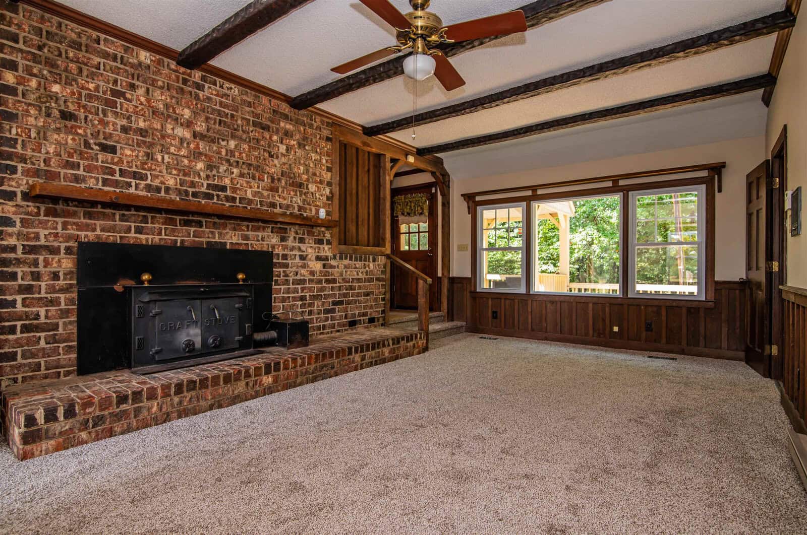 Spacious room with brick fireplace, beige carpet, wooden trim, and a bay window allowing natural light.