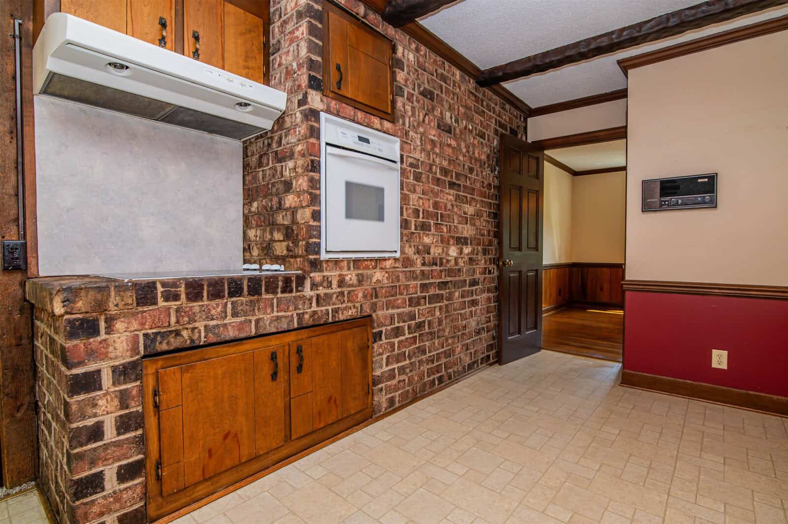 A dated kitchen interior featuring brick walls, wooden cabinets, and older appliances.