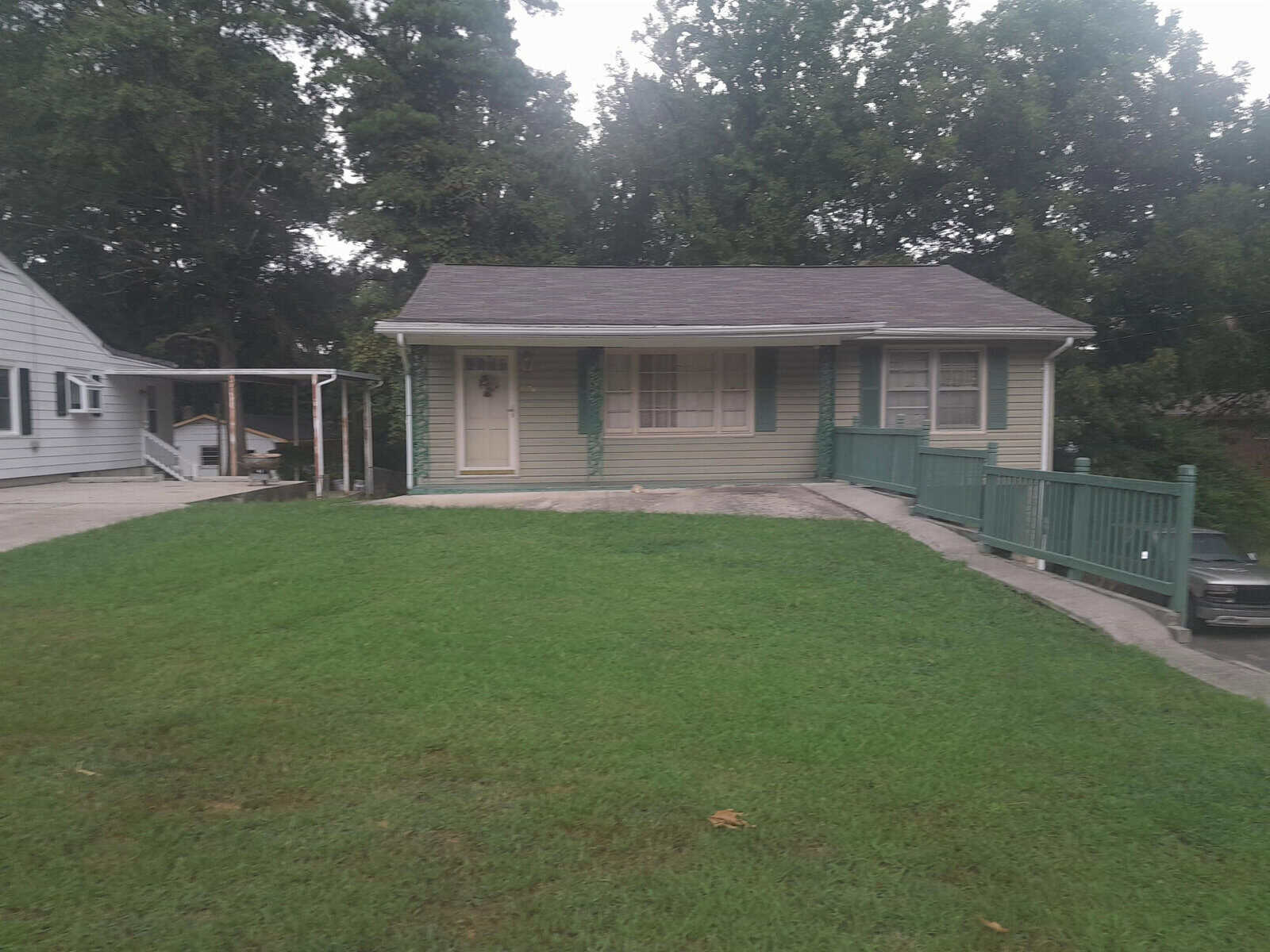 A single-story house with a green trim, a front porch with railings, and a well-maintained lawn in front.