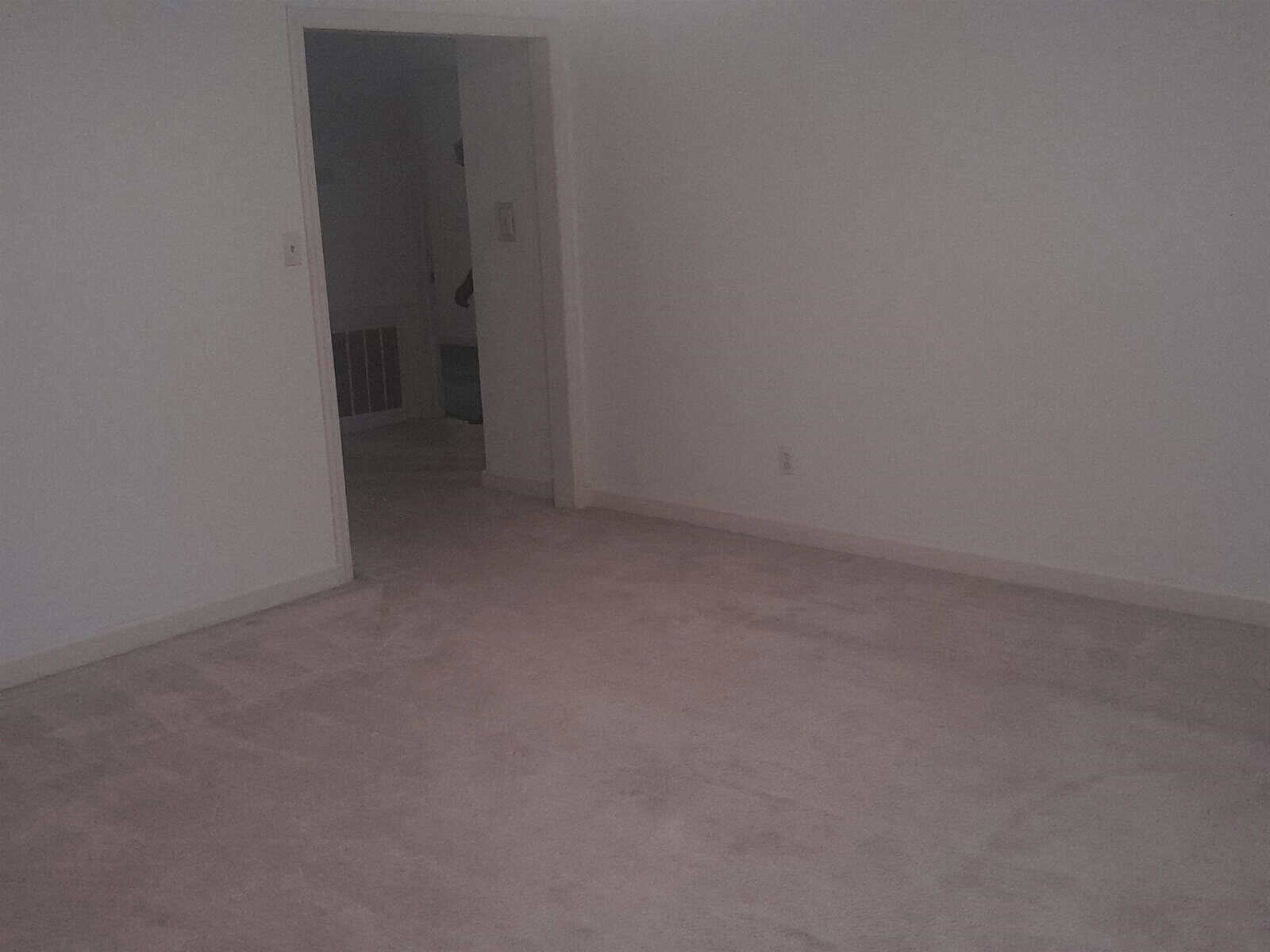 An empty room with light-colored carpet flooring and white walls, featuring an open doorway leading to another area with a visible stair railing.