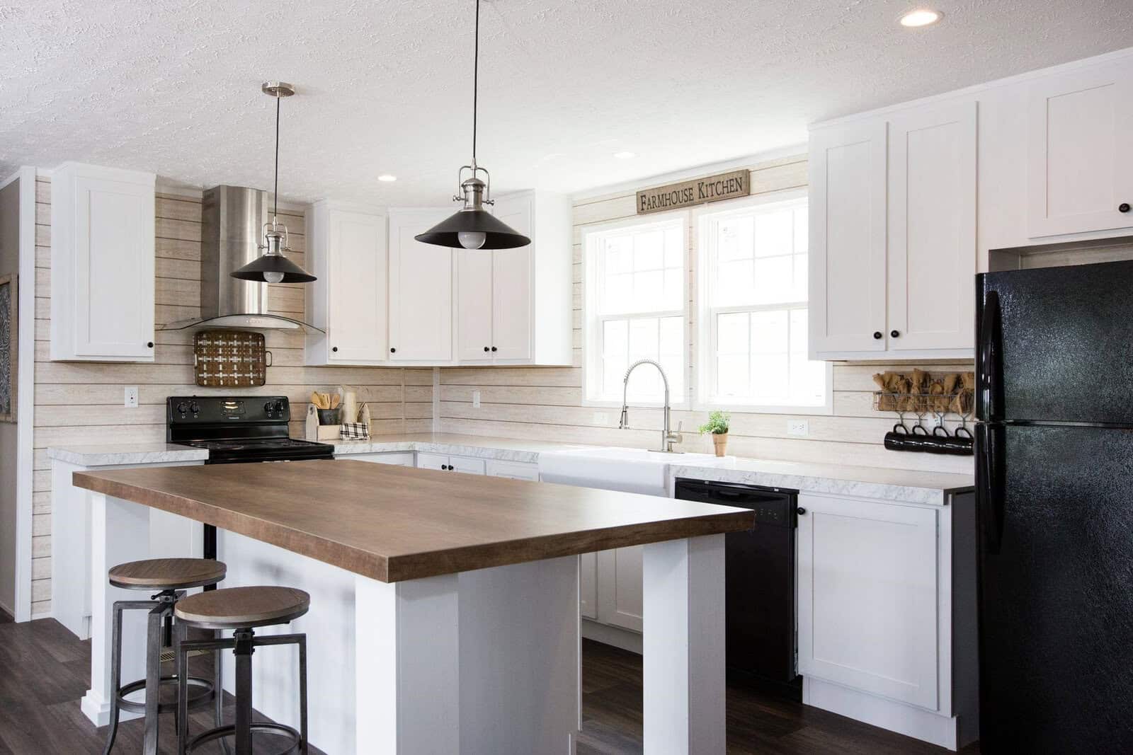 A modern kitchen interior with white cabinets, a central island with a wooden countertop, black appliances, and pendant lights.