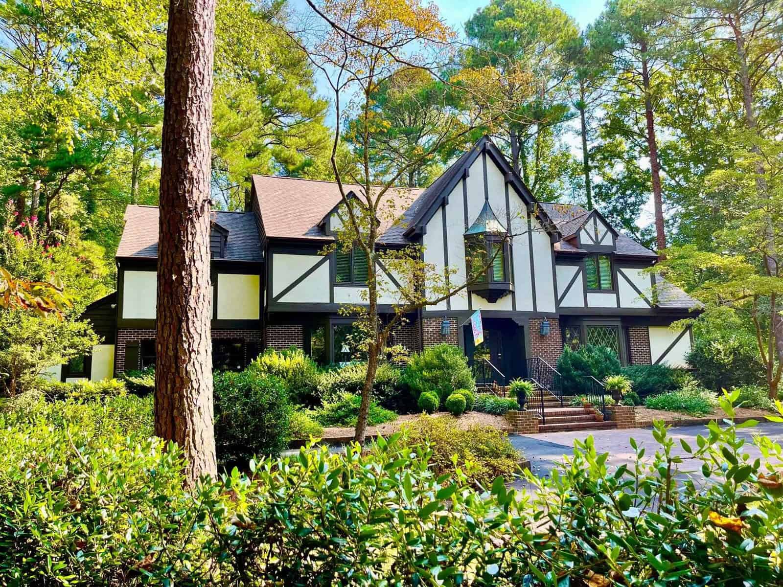 A tudor-style house nestled among trees with a well-maintained garden and a brick-paved driveway.