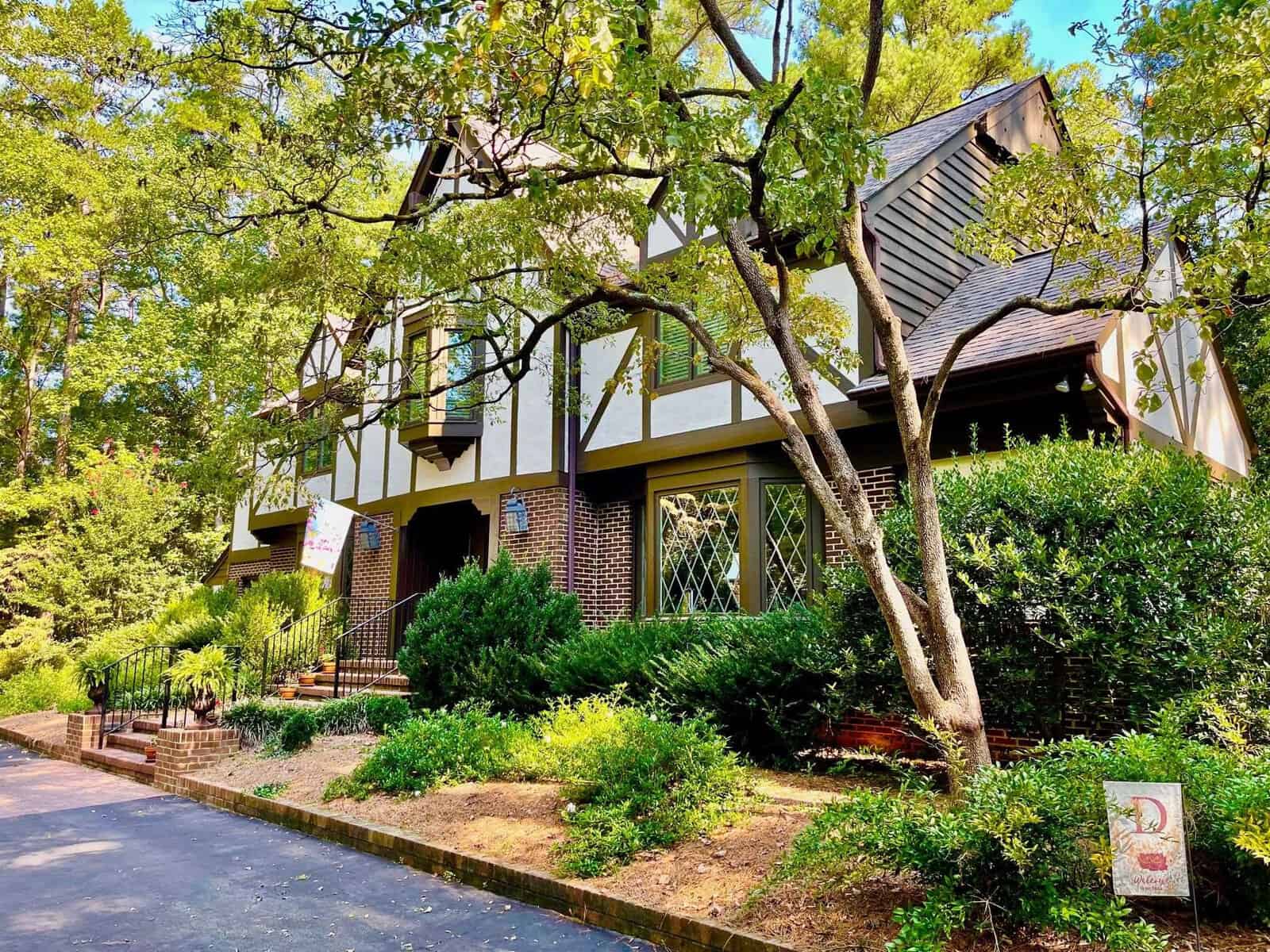 A tudor-style suburban house surrounded by lush greenery on a sunny day.