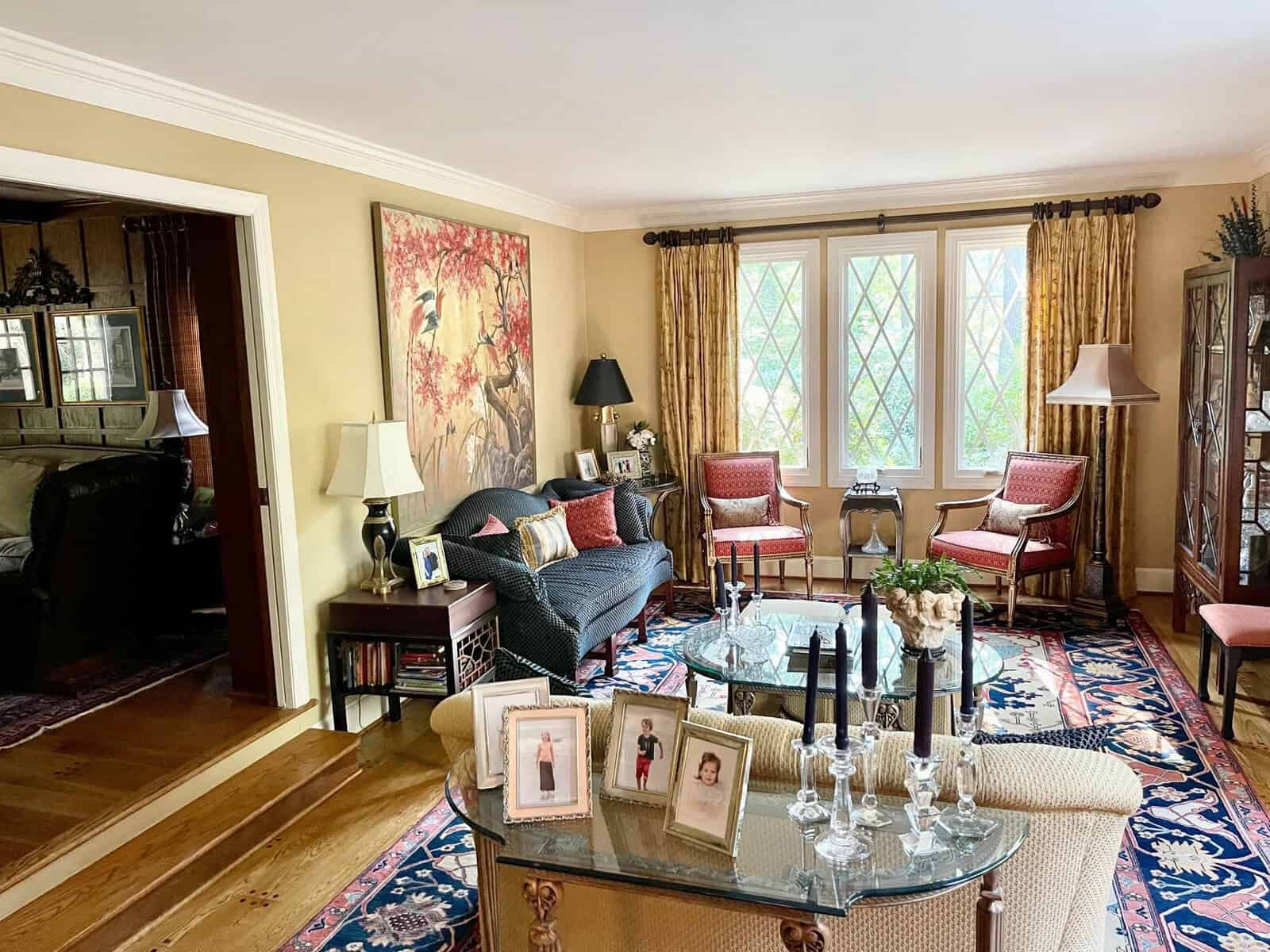 A traditionally decorated living room with a seating arrangement that includes a sofa and several chairs, a coffee table adorned with candles, and a prominent red-accented artwork on the wall.