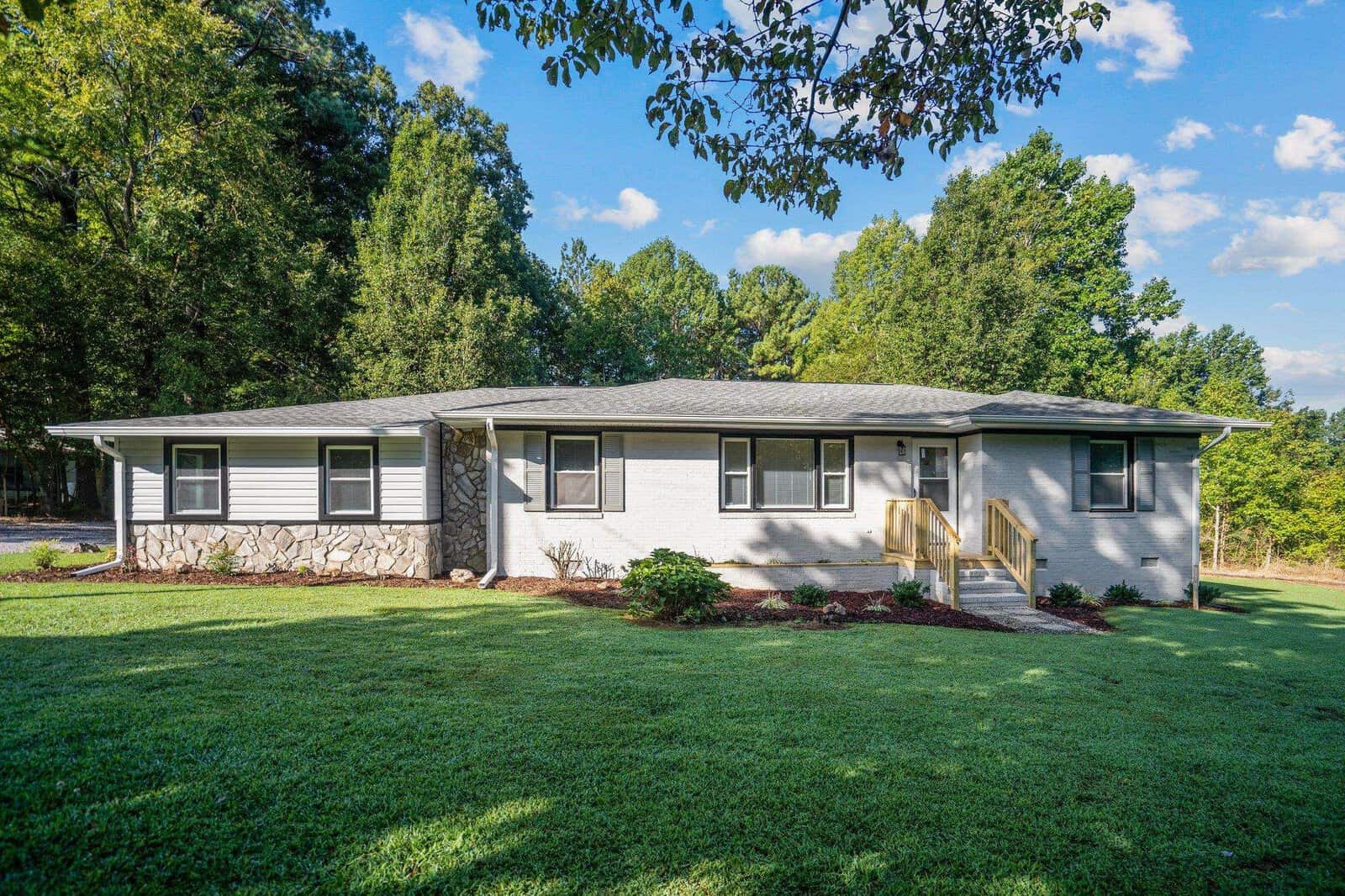 A single-story home with a well-manicured lawn and surrounding trees on a sunny day.