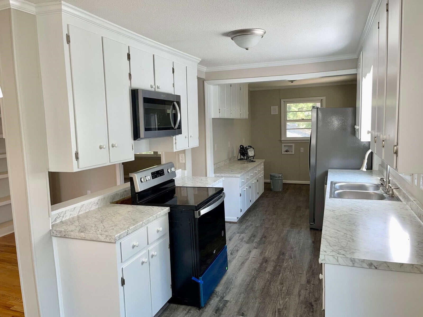 A clean, modern kitchen with white cabinetry, stainless steel appliances, marble countertops, and gray flooring. bright natural light fills the space.