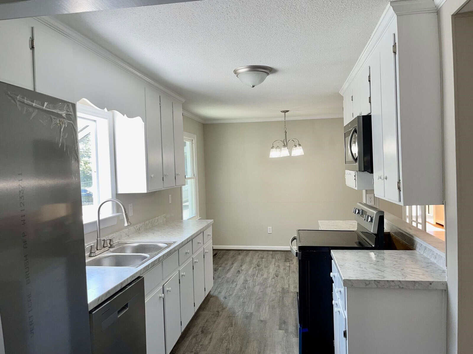 Modern kitchen with white cabinetry, stainless steel appliances, and gray flooring. key features include a double sink, microwave above the stove, and an island with a black countertop. bright and airy space.