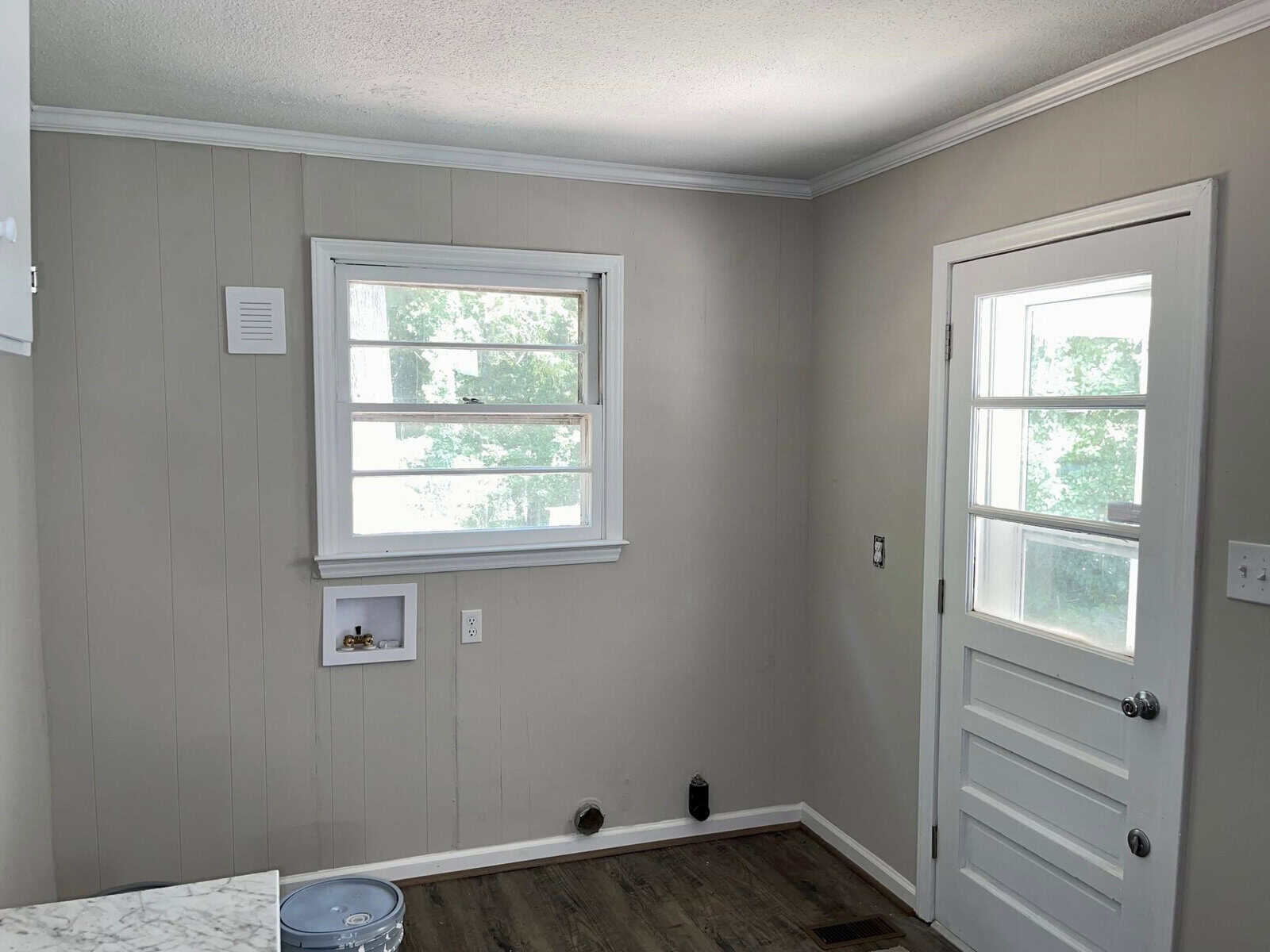 A small, tidy room with gray walls and white trim. it includes two windows, a white door, and a marble countertop. a photo frame and vent are visible on one wall.