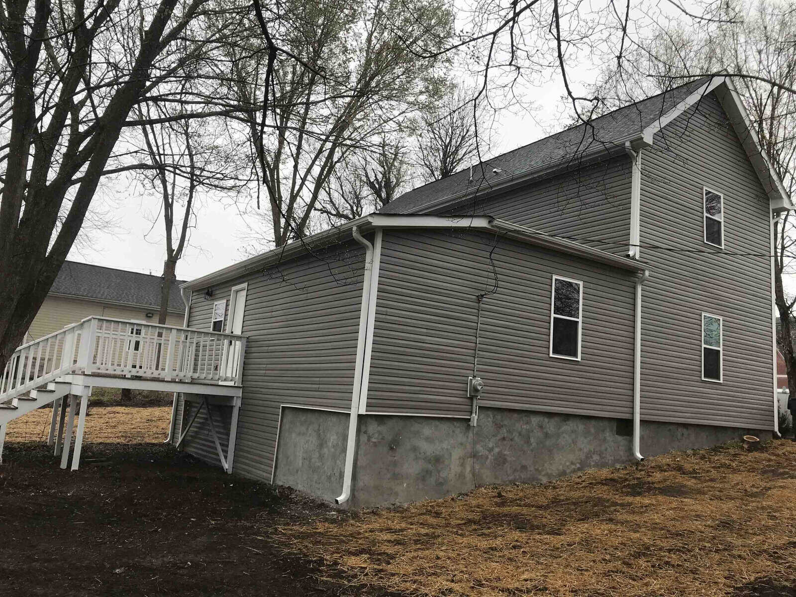 A two-story house with vinyl siding and a small wooden deck on an overcast day.