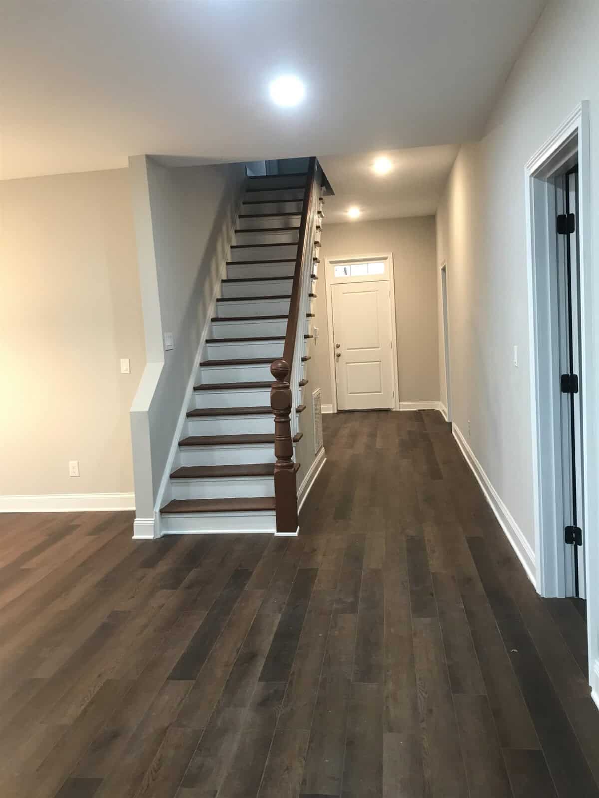 A staircase in a residential home with wooden balusters and handrail, leading from a laminate floored hallway with white walls and closed doors on the side.