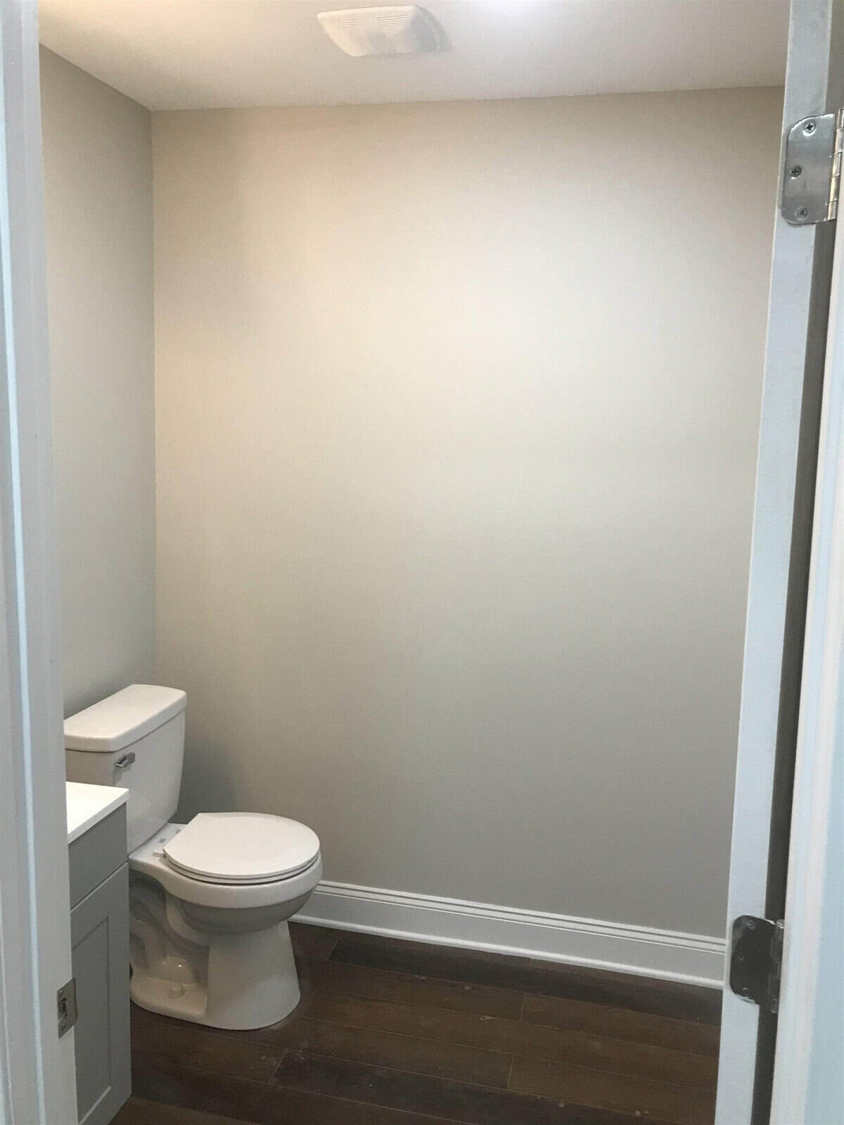 A small, modern bathroom featuring a closed toilet seat next to a sink cabinet, with tiled flooring and a neutral wall color, viewed from an open doorway.