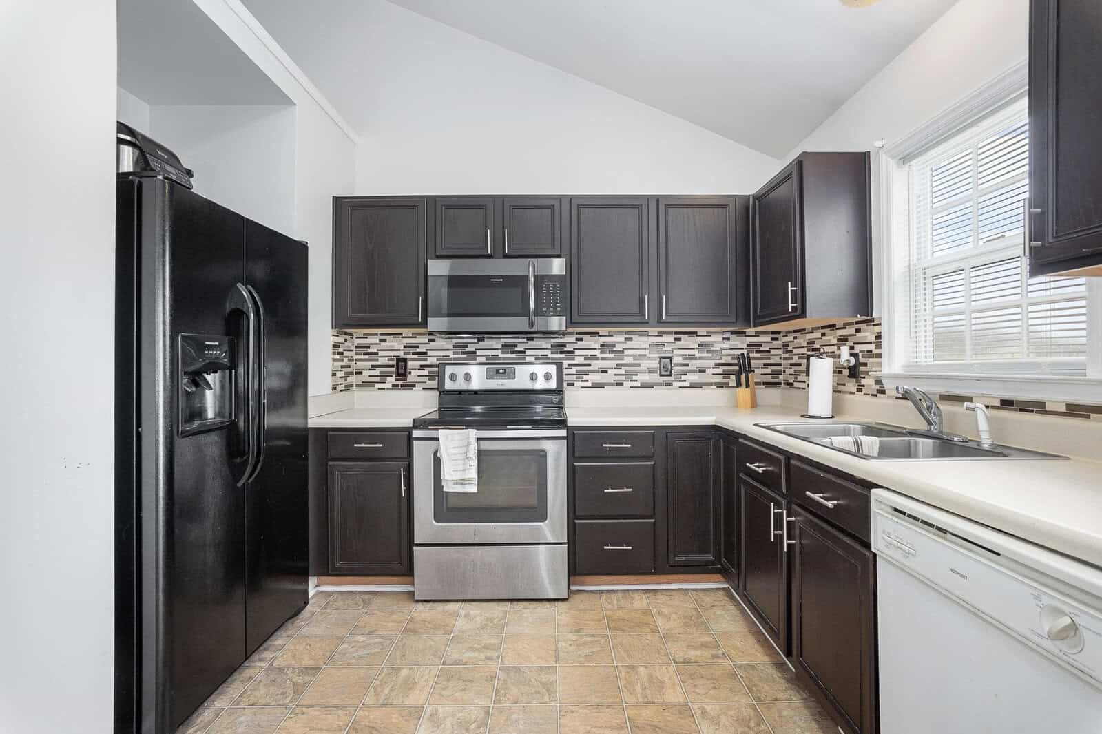 A modern kitchen with black appliances, dark cabinetry, and a mosaic backsplash.