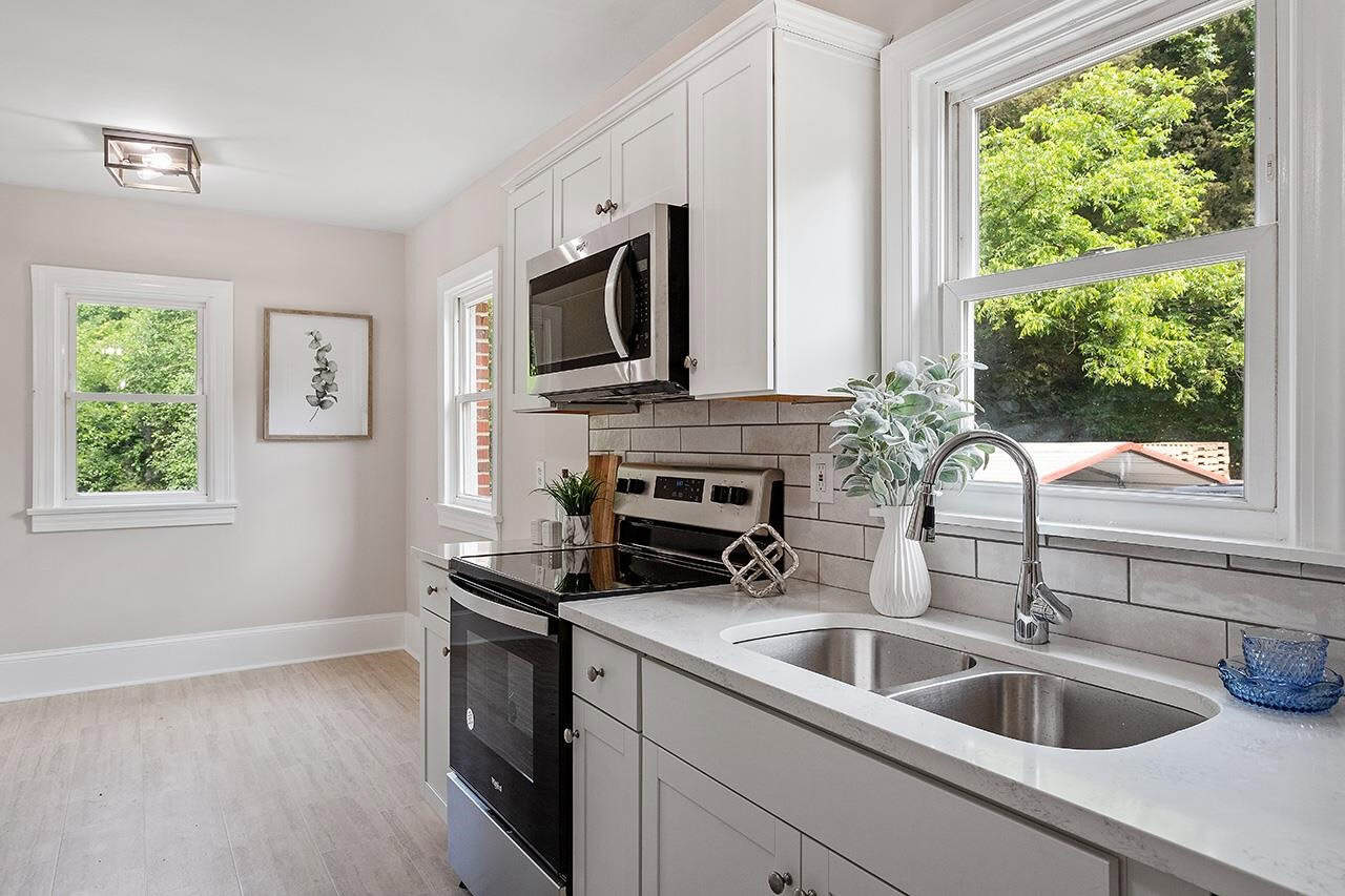 A modern kitchen with white cabinetry, stainless steel appliances, a double sink, and a window providing natural light.
