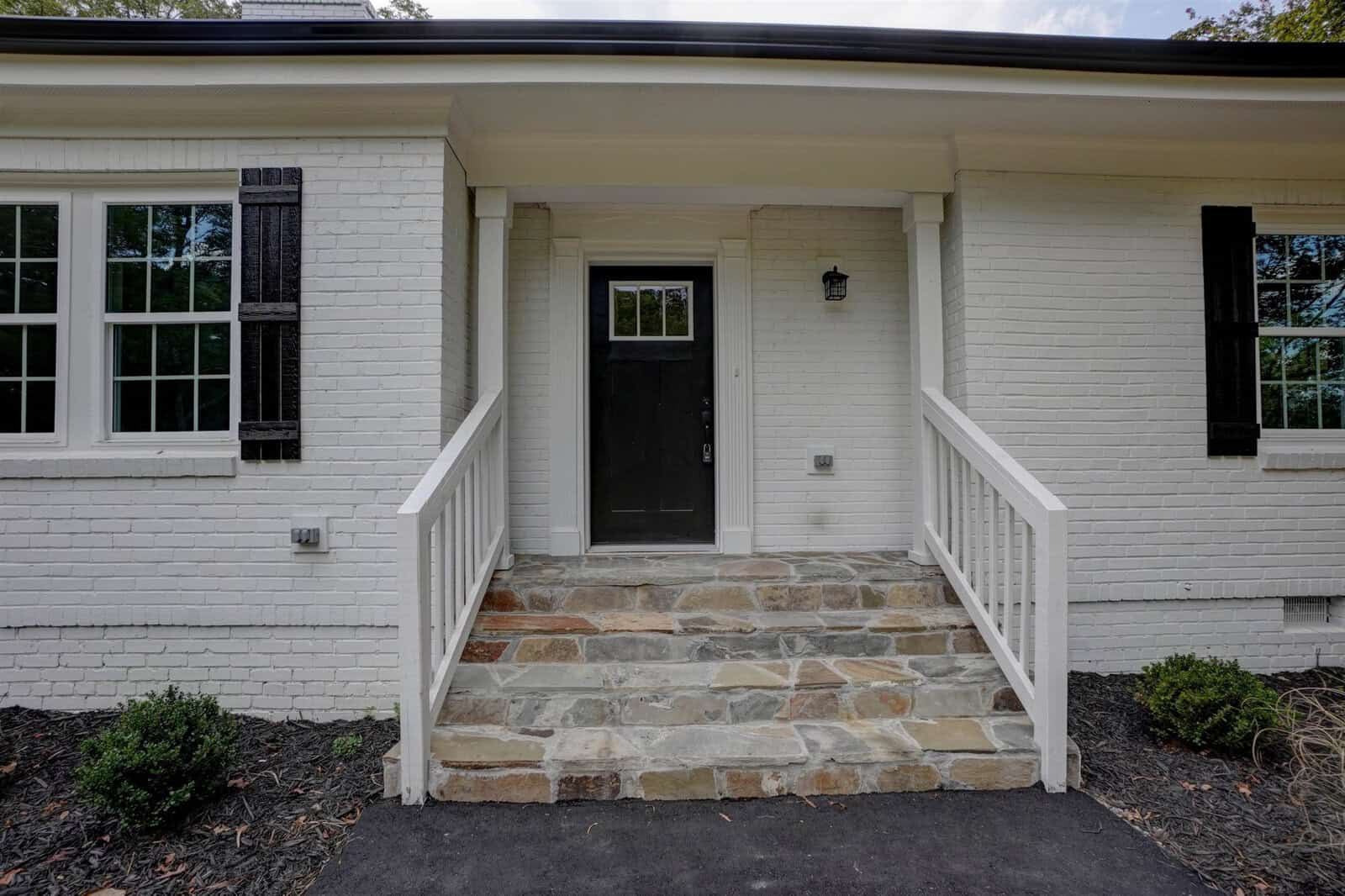 White brick house with a black front door and stone steps leading up to a covered porch.