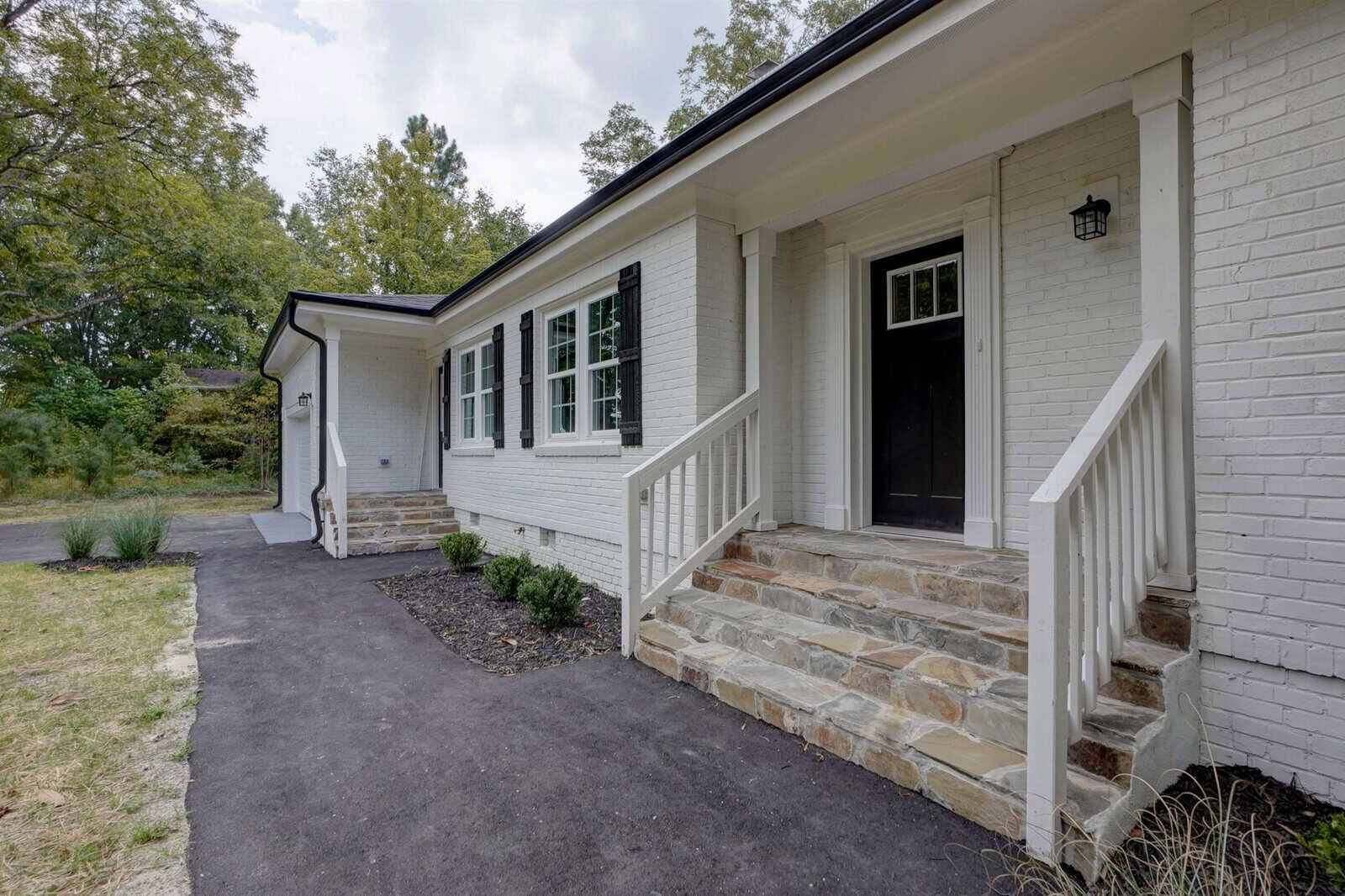 A newly renovated single-story house with white exterior brick walls, a black front door, and a porch with stone steps and white railings.
