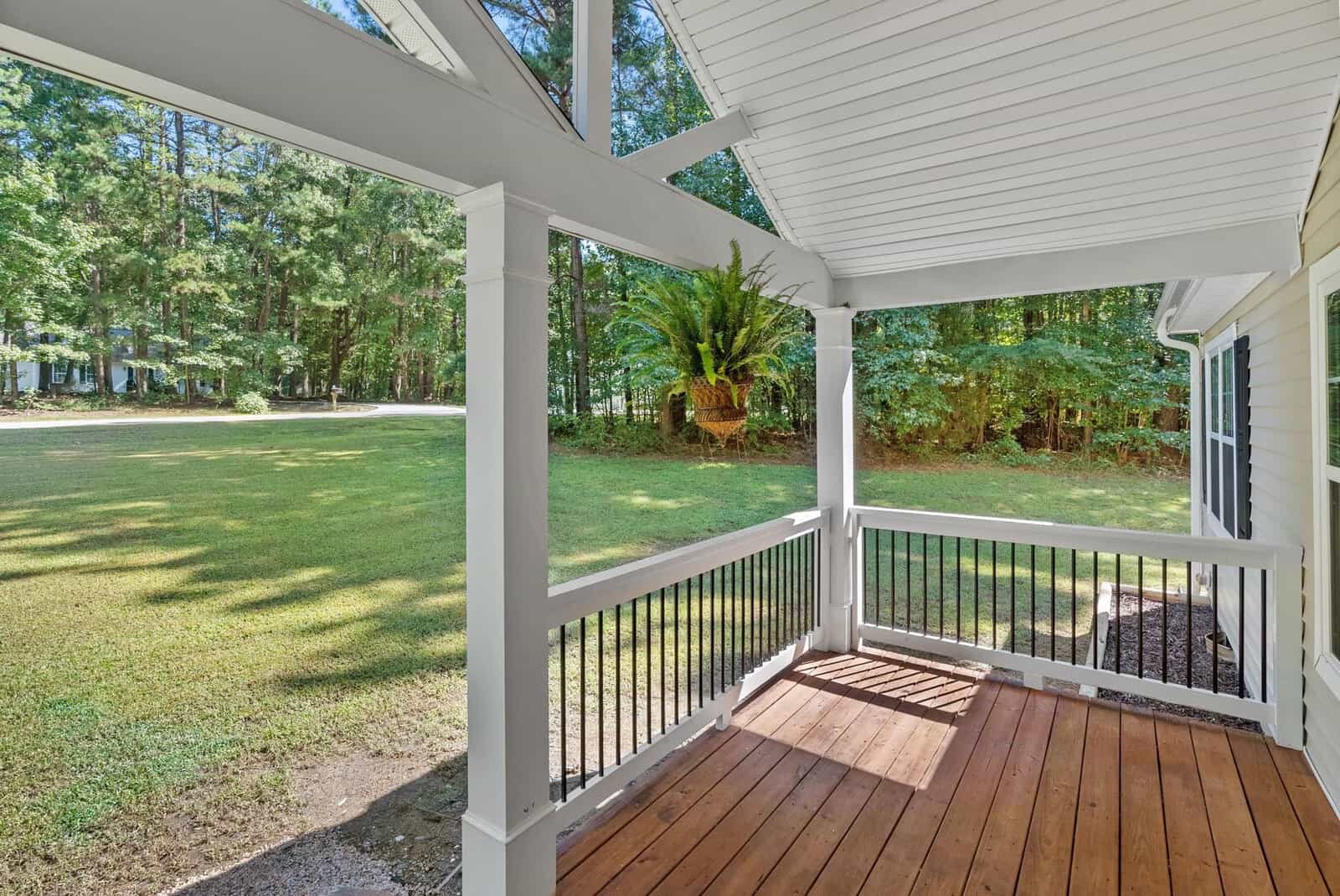 A wooden deck of a house overlooking a yard with green trees in daylight.