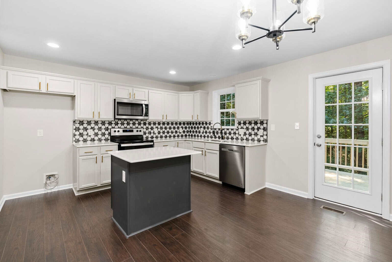 A modern kitchen with white cabinetry, stainless steel appliances, a central island, and a patterned backsplash, featuring hardwood floors and a door leading to the outside.