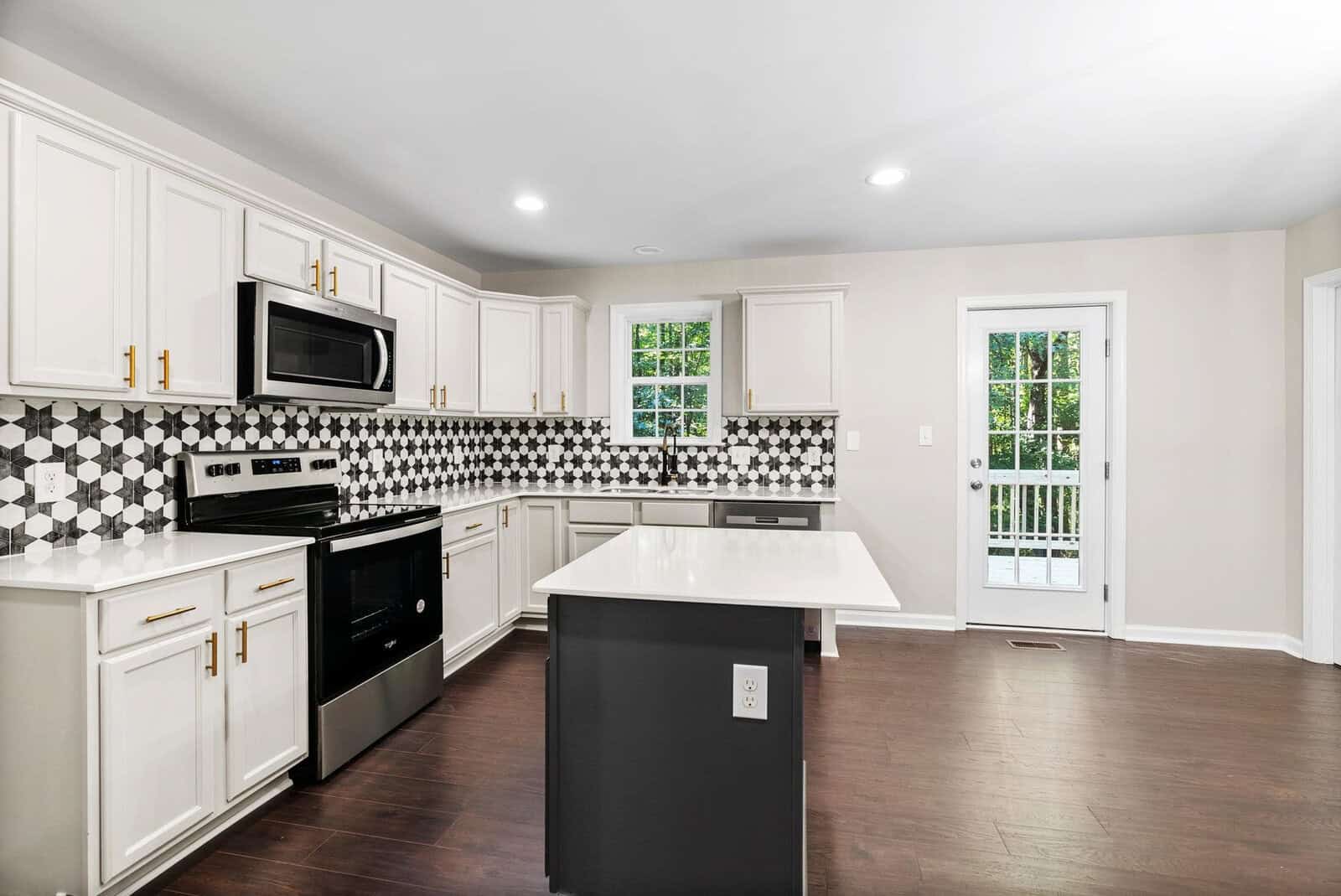 A modern kitchen with white cabinetry, stainless steel appliances, a patterned backsplash, and a central island, leading to a door with a view of the outside.