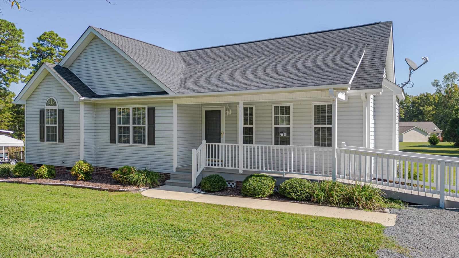 Charming single-story white house at 2514 Wes Sandling Road, Franklinton, with gray roof, front porch, and wheelchair-accessible ramp. Grassy yard features small shrubs; satellite dish on the roof. Trees and another house visible in the background.