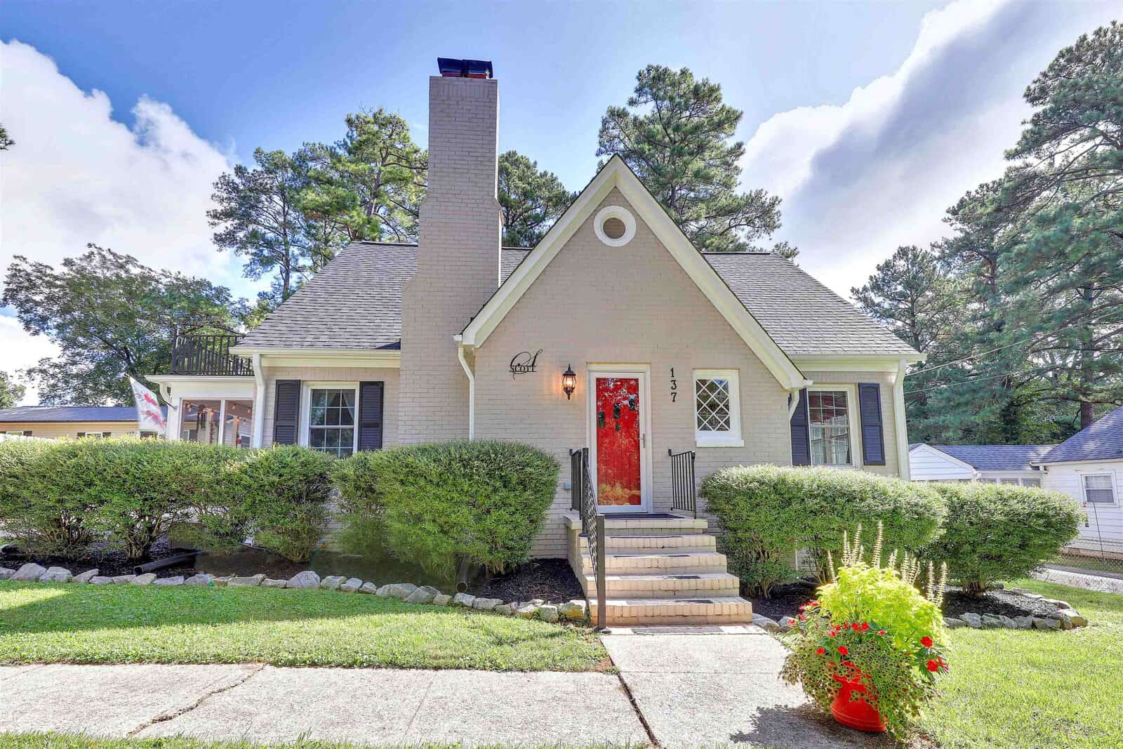 A well-kept suburban home with a gabled roof, featuring a red front door, neat shrubbery, and a clear blue sky in the background.
