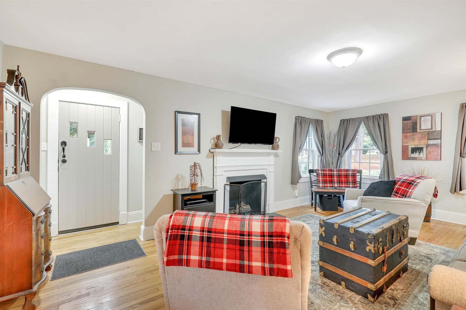 A cozy living room featuring a fireplace with a mounted television above, a white entry door, two sofas with plaid accents, and hardwood flooring.