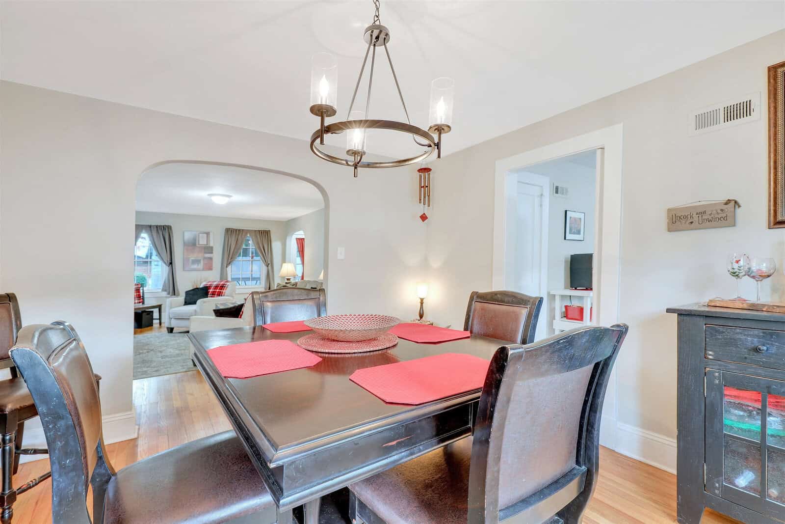 A well-lit dining room featuring a dark wood table with place settings, complemented by a chandelier above and an open archway leading to another room.