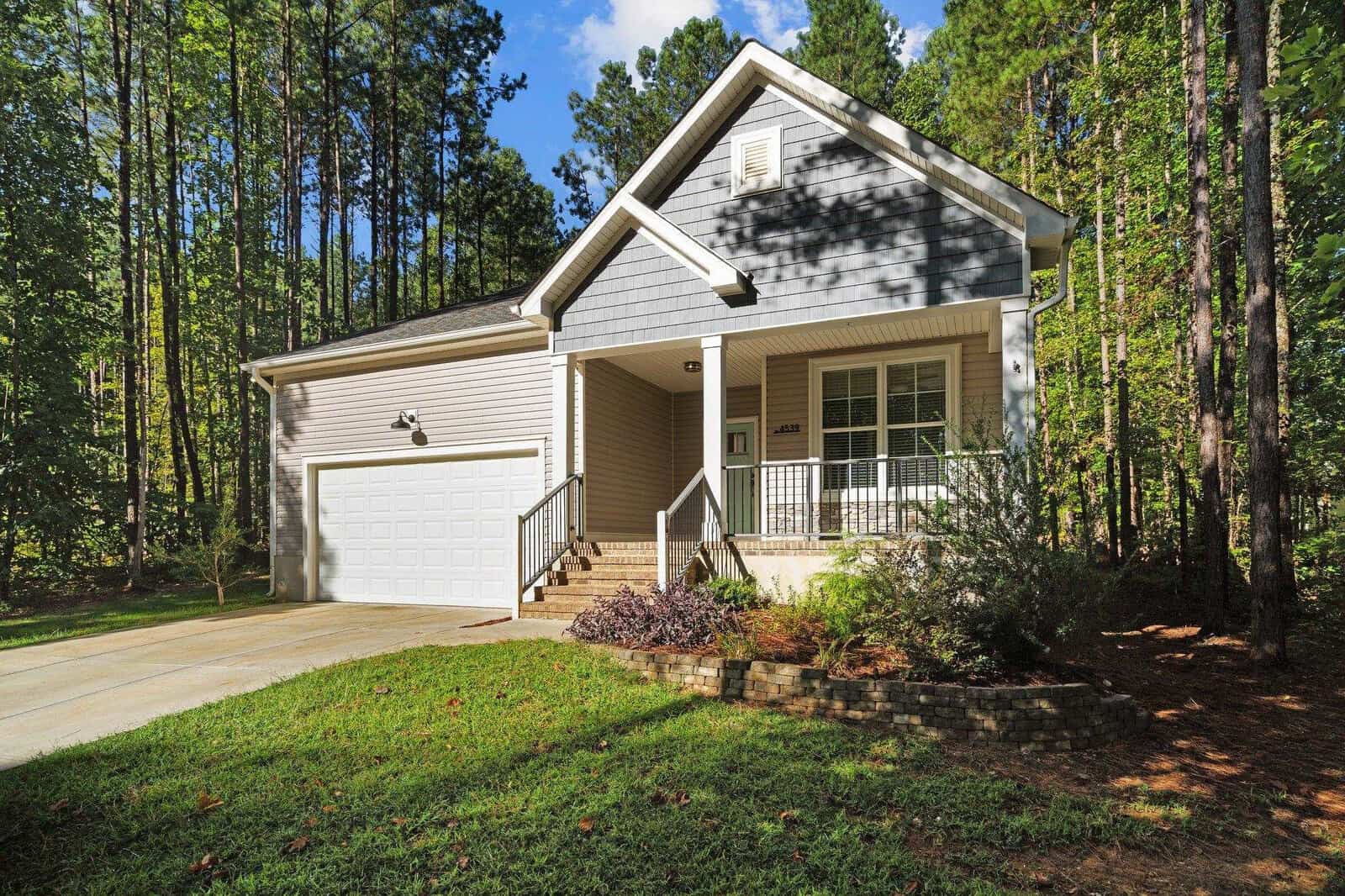A modern gray house with white trim and a two-car garage, located at 4539 Gresham Drive in Oxford, is surrounded by lush green trees. It features a small front porch with steps leading up and a neatly manicured lawn. The sky above is blue with a few clouds.