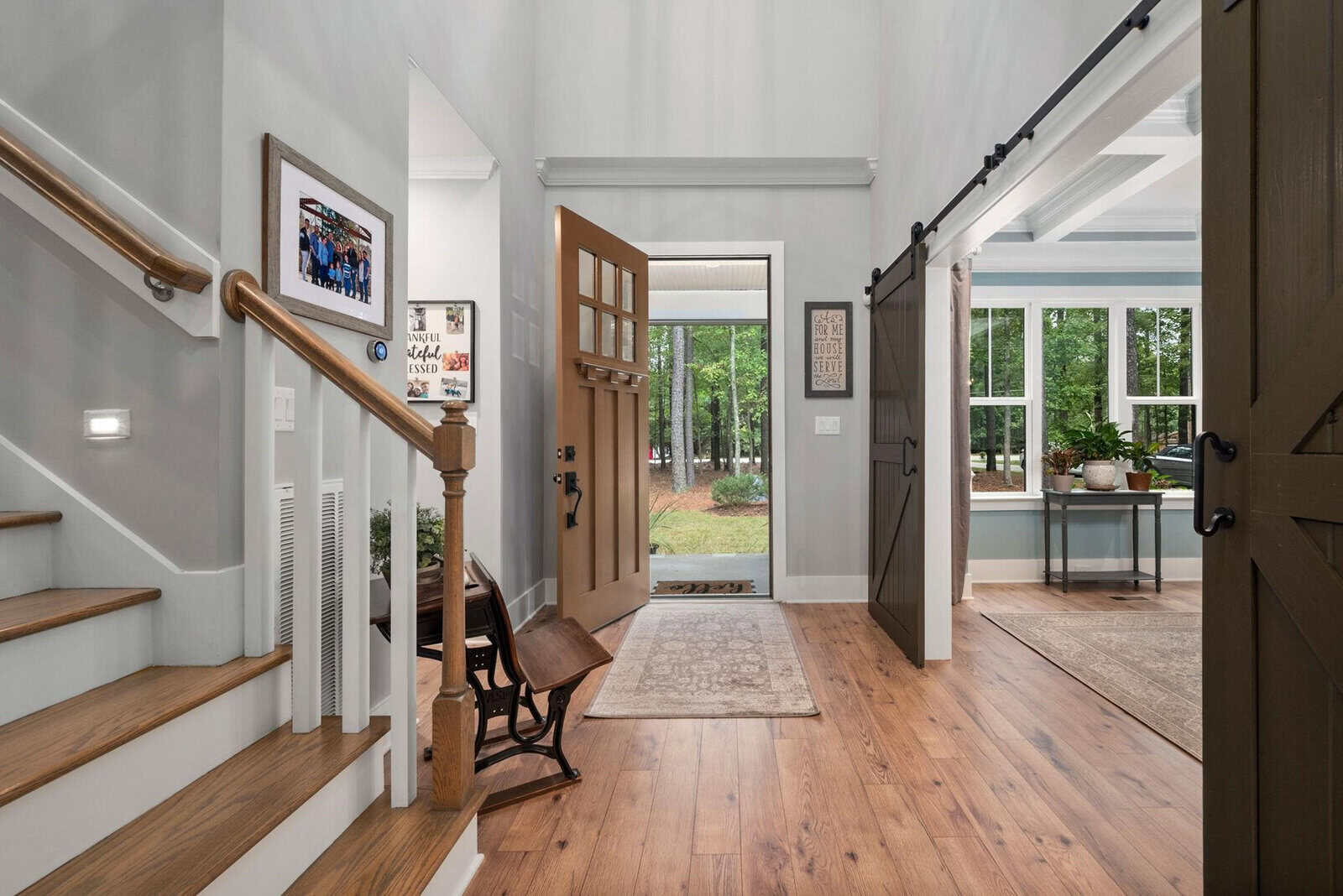 A welcoming foyer with a wooden floor greets you at 604 Lawrence Road, Wake Forest. An open front door and staircase to the left set the tone, while barn-style sliding doors reveal a bright room with large windows. A small rocking chair sits nearby, and framed pictures adorn the walls.