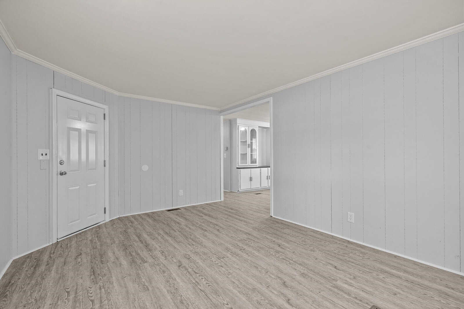 An empty room with gray walls and laminate flooring featuring an open doorway leading to an adjacent room.