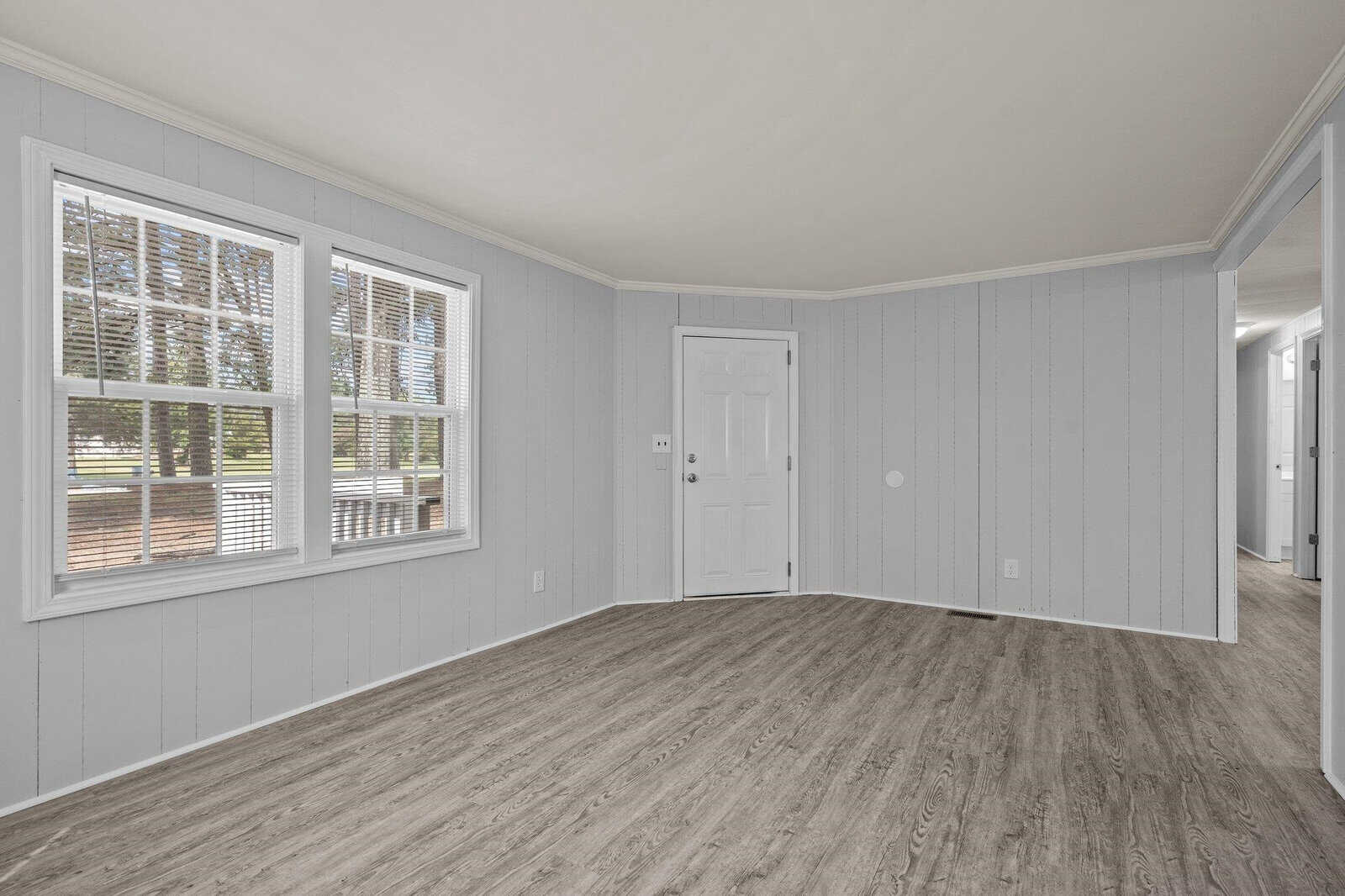 An empty room with light blue walls and wood laminate flooring featuring two windows with blinds and a white front door.