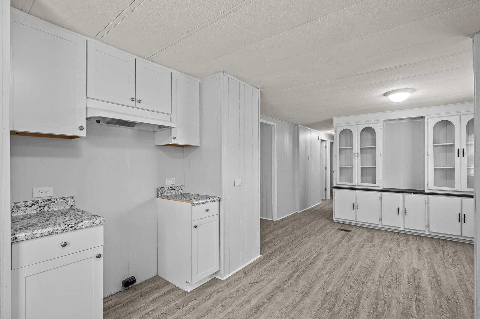 Modern kitchen interior with white cabinets, granite countertops, and wood laminate flooring in a house.